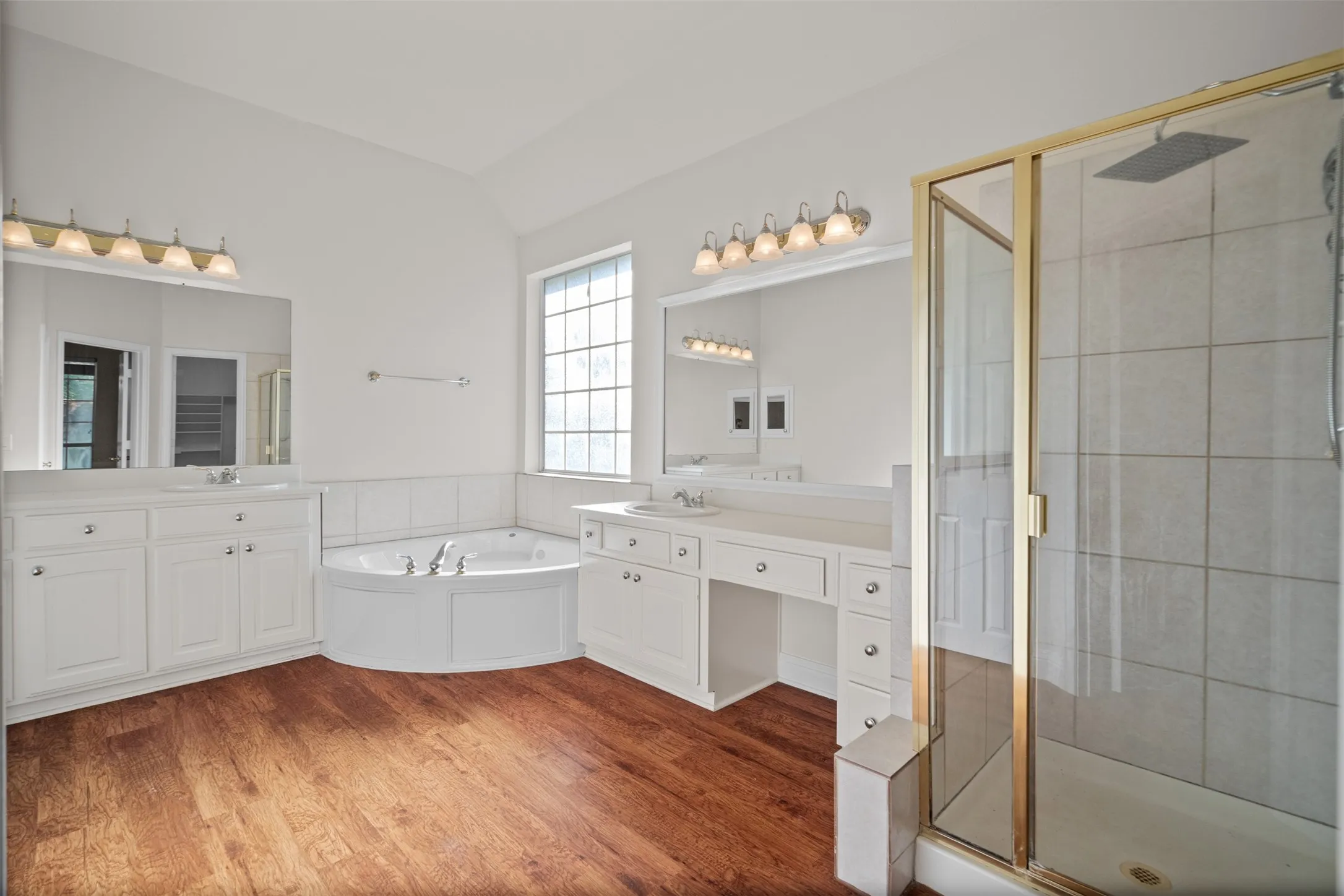 Vaulted ceiling, wood-finish flooring, corner soaking tub, dual vanities, and a glass-enclosed shower