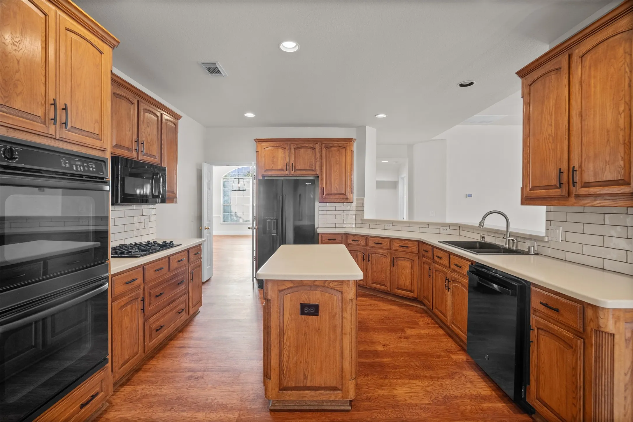 Kitchen featuring extensive wood cabinetry, light-toned countertops, a central island, integrated double ovens, and a gas cooktop