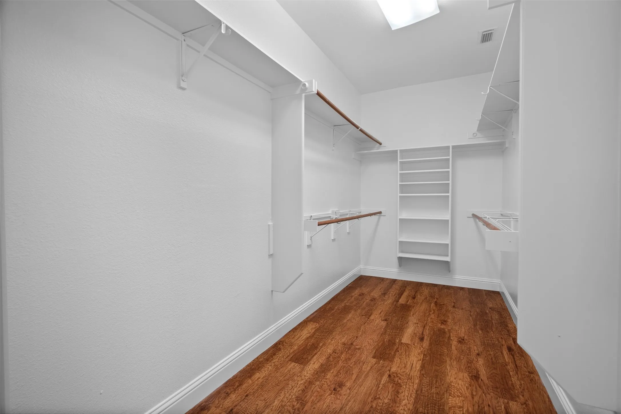 Walk-in closet featuring wood-finish flooring, built-in shelving, and multiple hanging rods