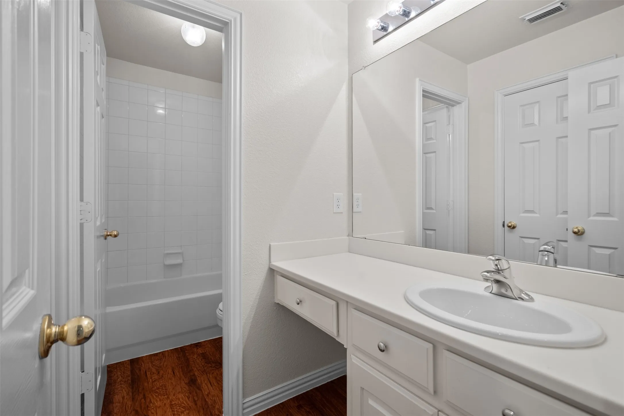 Bathroom featuring a vanity with an integrated sink, polished chrome faucet, full-width mirror, and wood-finish flooring