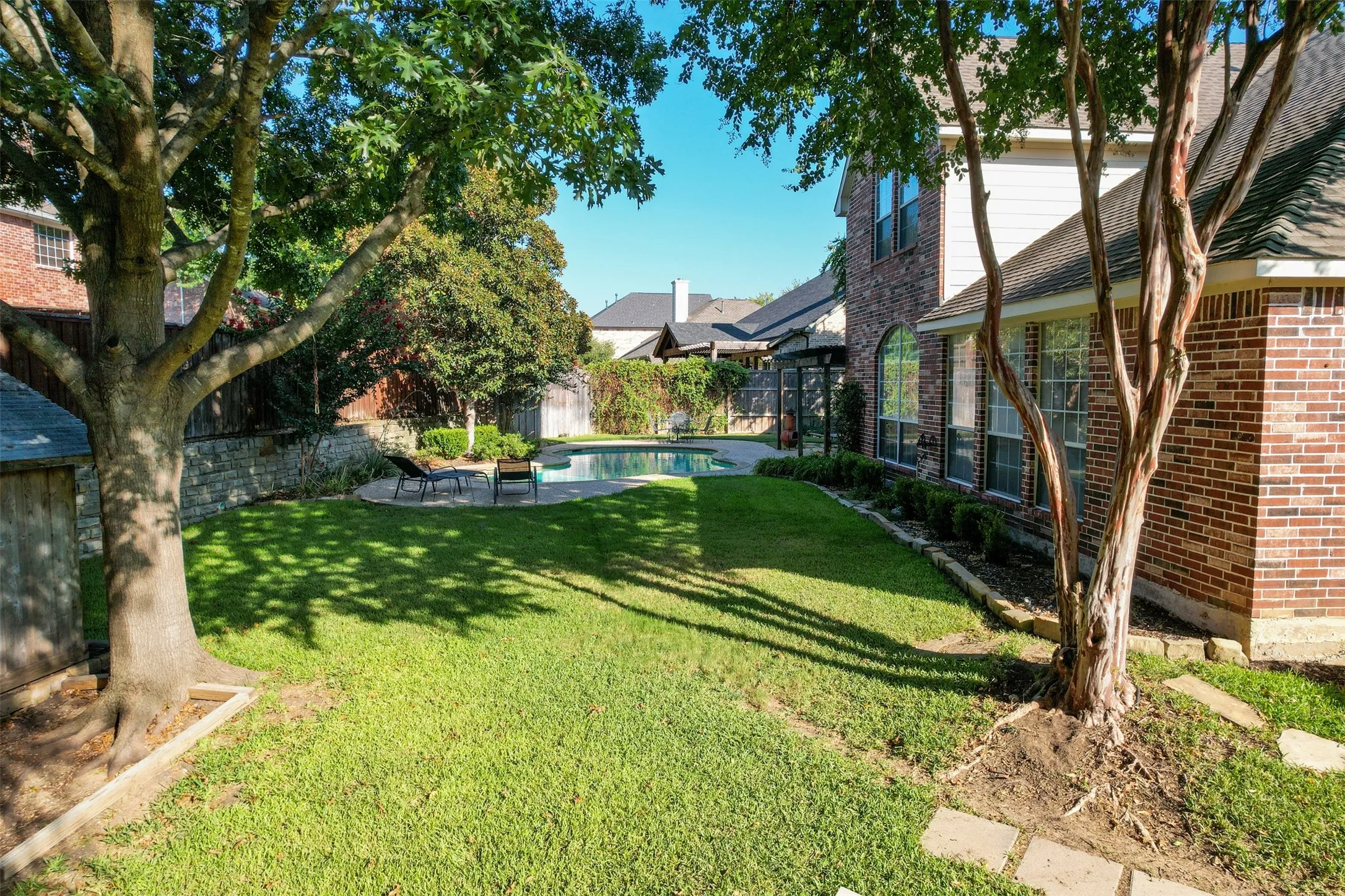 Expansive lawn area, brick-clad exterior, established trees, and built-in swimming pool with surrounding hardscaping