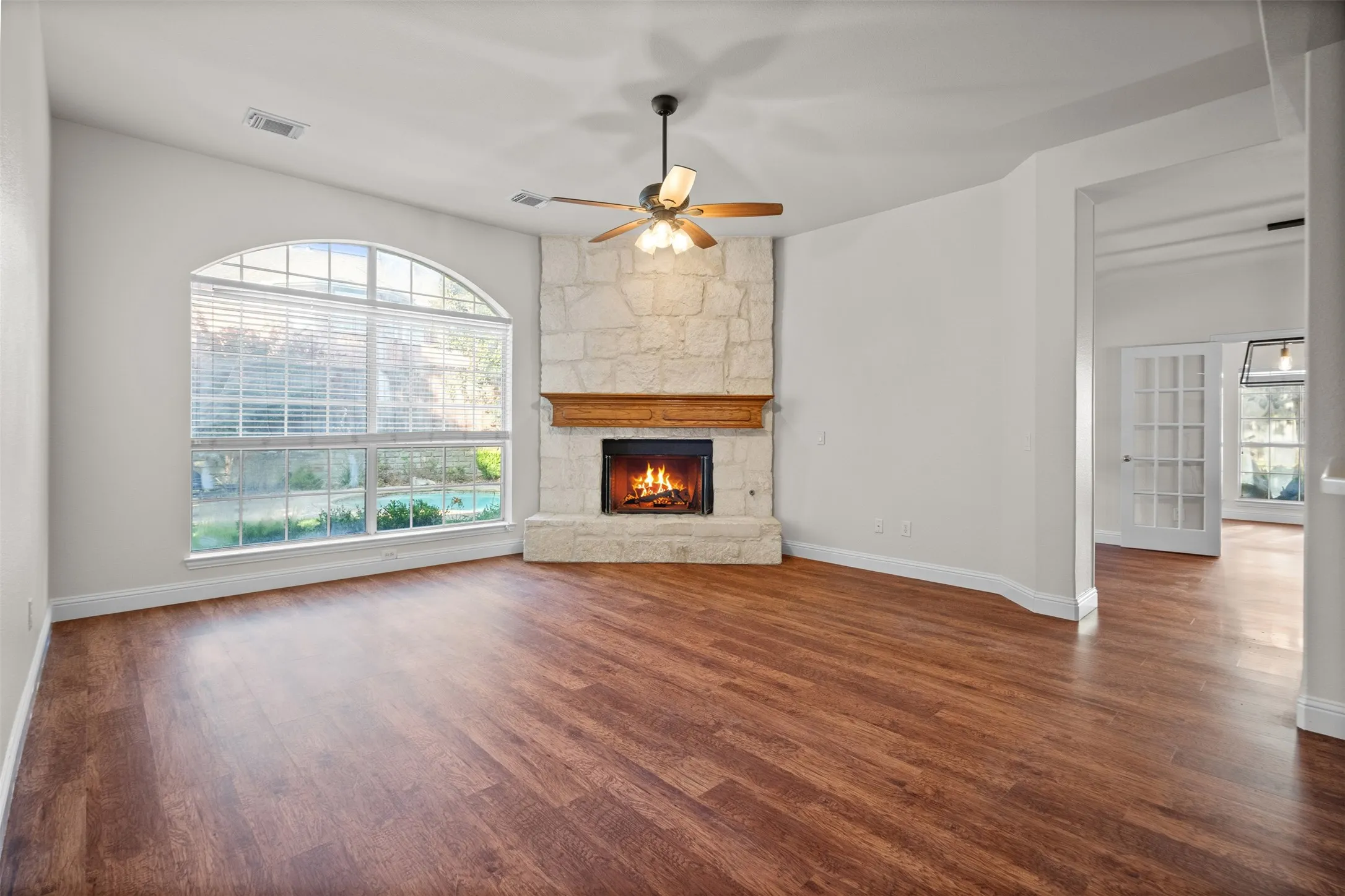 Vaulted ceiling, arched window with blinds, wood-finish flooring, stone-surround fireplace with wood mantel, and a ceiling fan