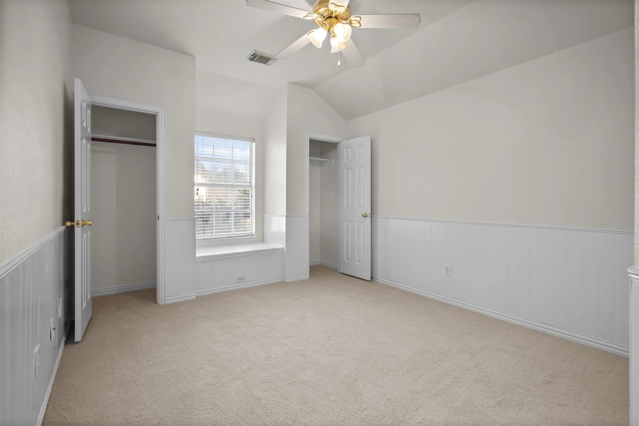 Vaulted ceiling with a ceiling fan light fixture, window with blinds, carpet flooring, and wainscoting