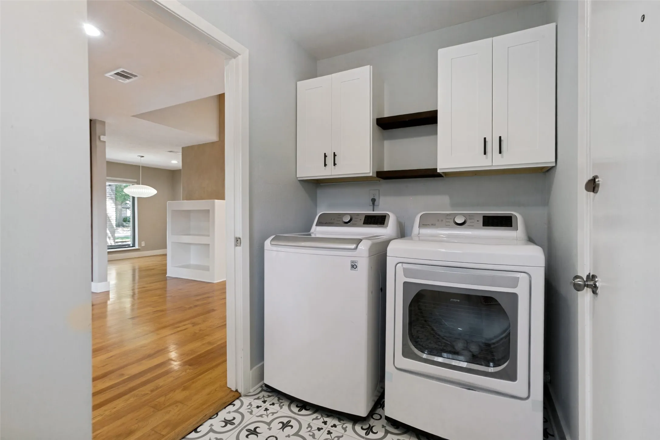 Laundry area with patterned floor tile, white shaker-style cabinetry, and wood-finish shelving