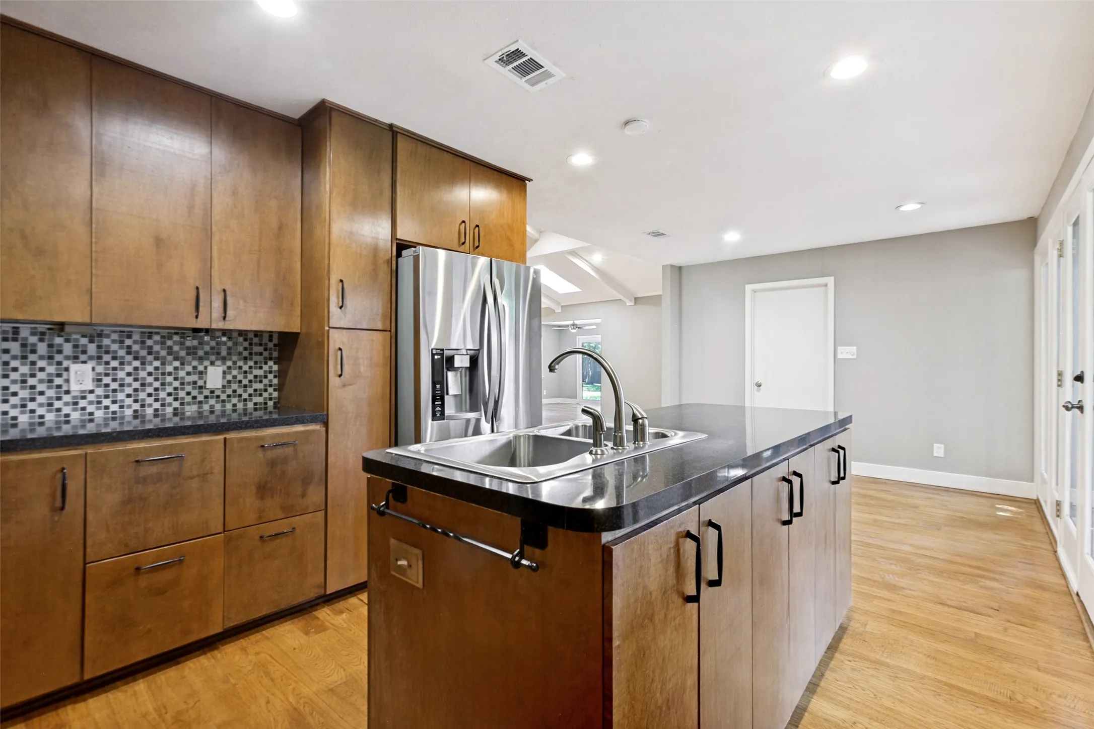 Kitchen featuring wood cabinetry, stainless steel appliances, a center island with sink, mosaic tile backsplash, and light wood-finish flooring