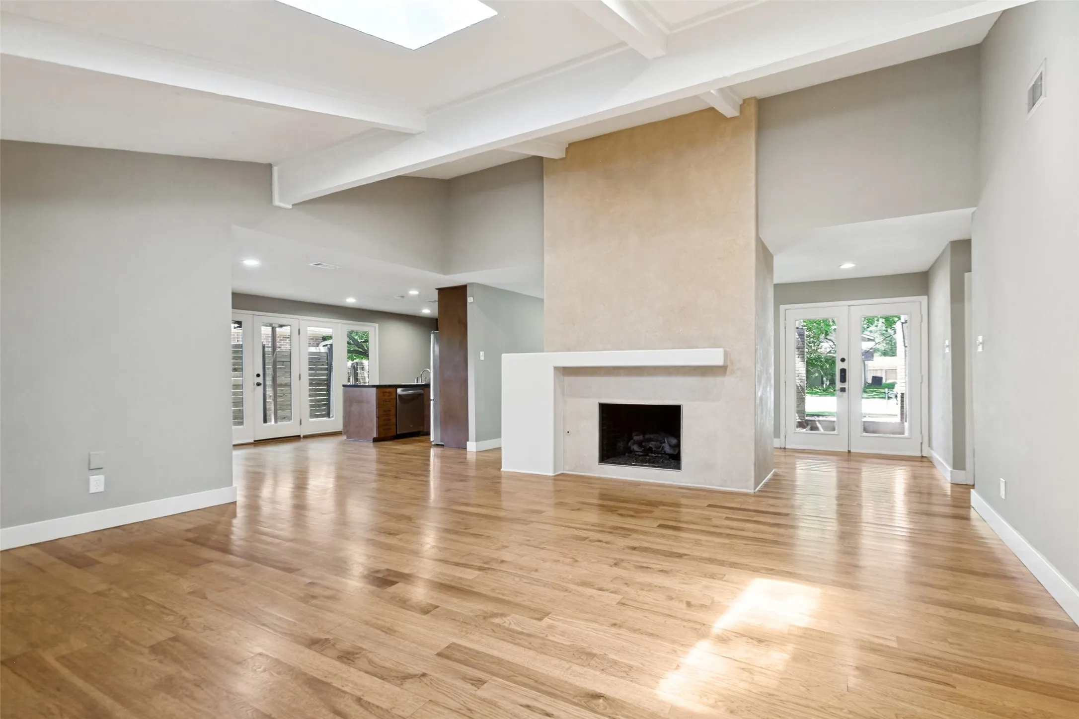 Hardwood flooring, central fireplace with mantle, exposed beam ceiling, recessed lighting, and a skylight
