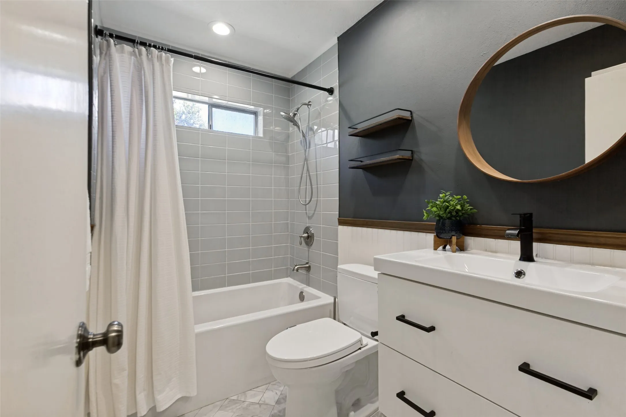 White vanity with matte black hardware, black wall-mounted faucet, and a round wood-frame mirror