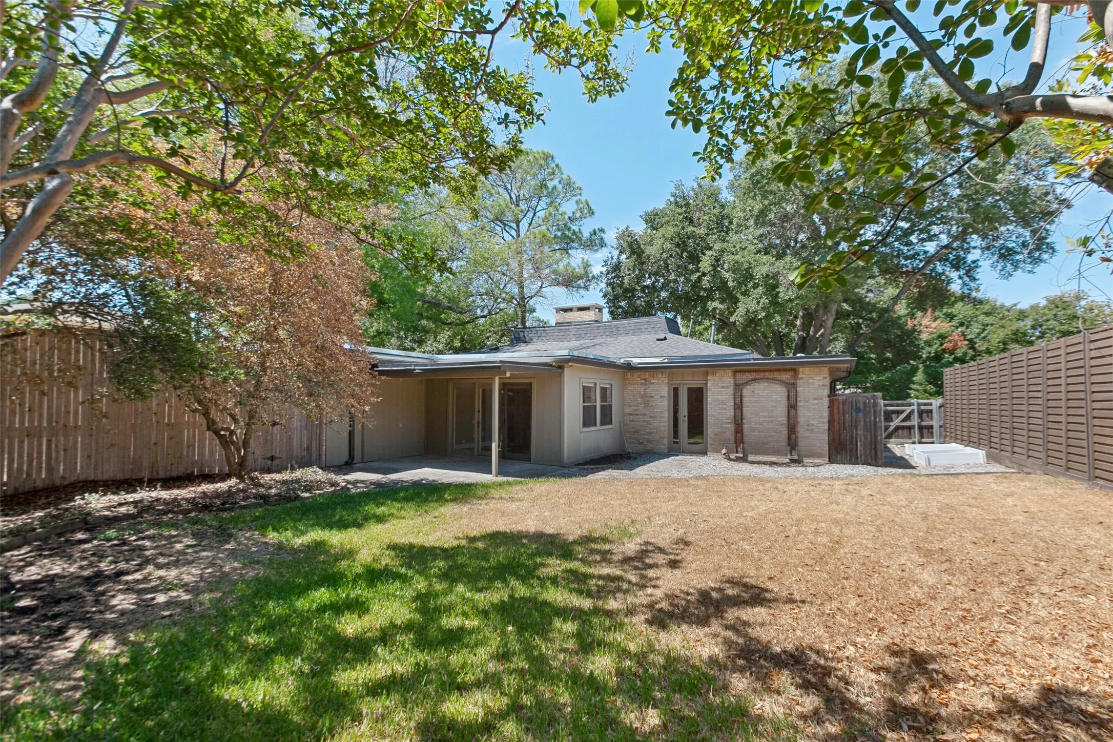 Expansive backyard with a partial grass lawn, mature trees, and a concrete patio