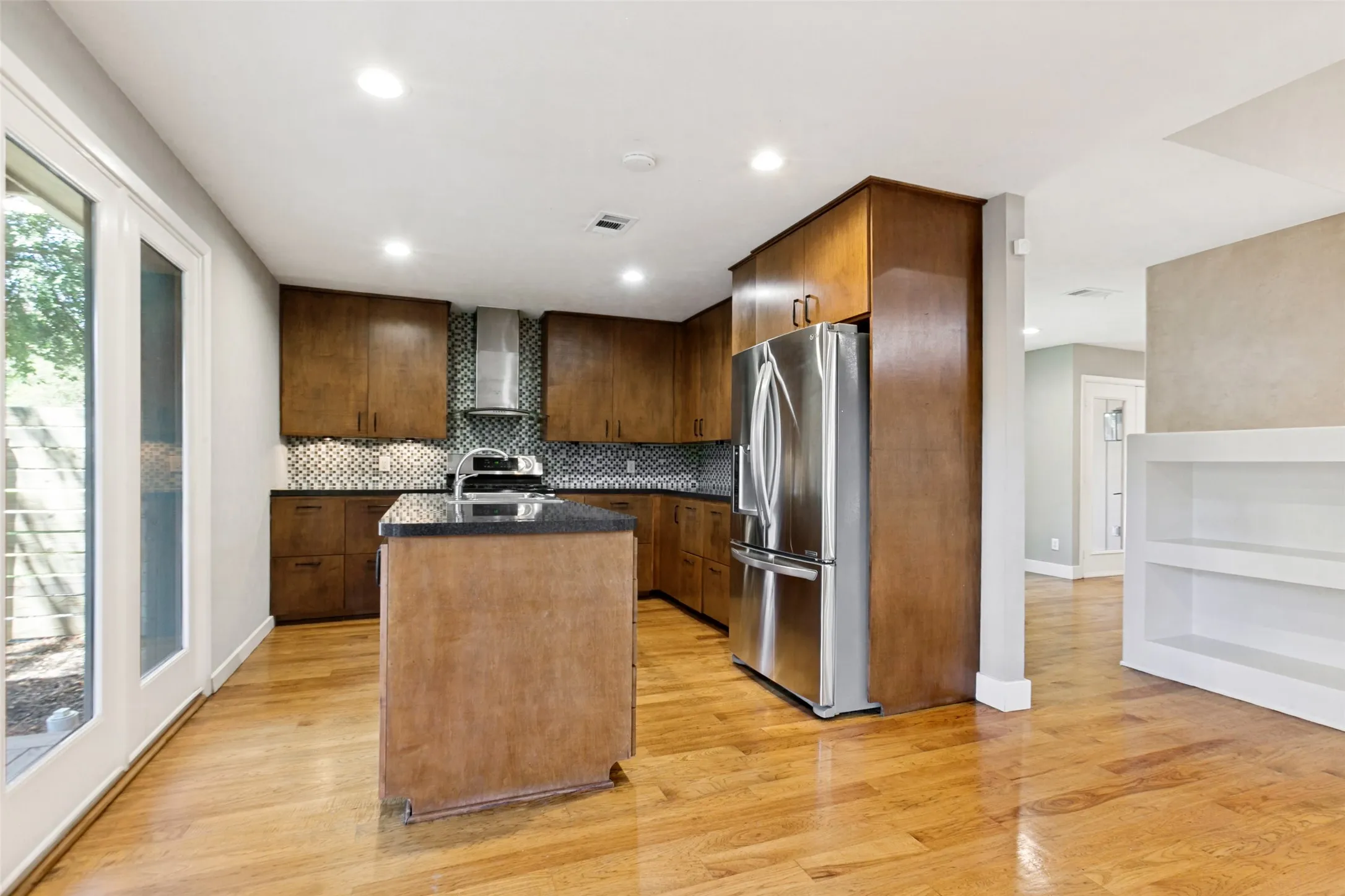 Kitchen featuring wood cabinetry, stainless steel appliances, a center island with a dark countertop, a patterned tile backsplash, and wood-finish flooring