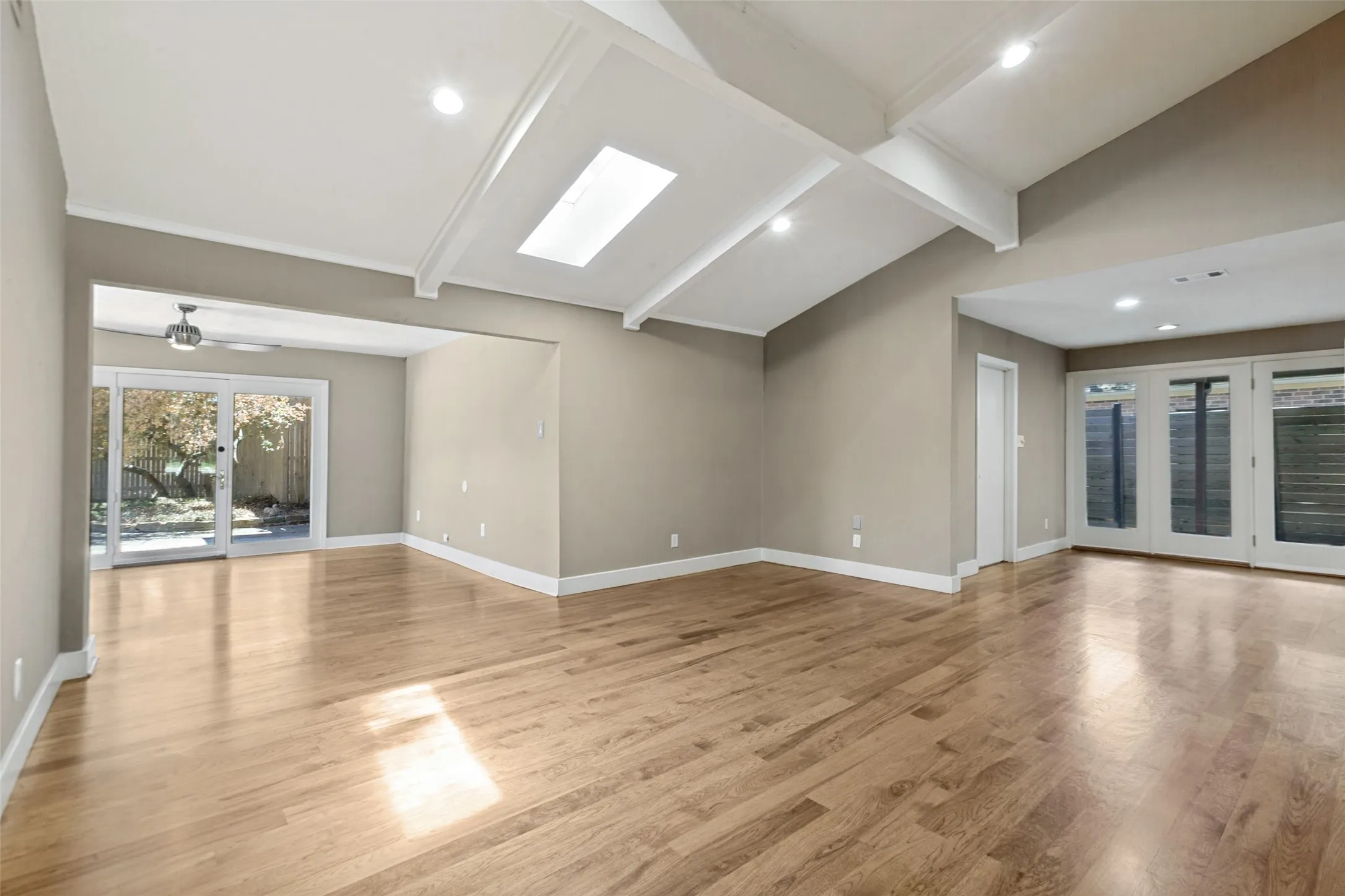 Vaulted ceiling with exposed beams, skylight, recessed lighting, wood-finish flooring, and sliding glass doors