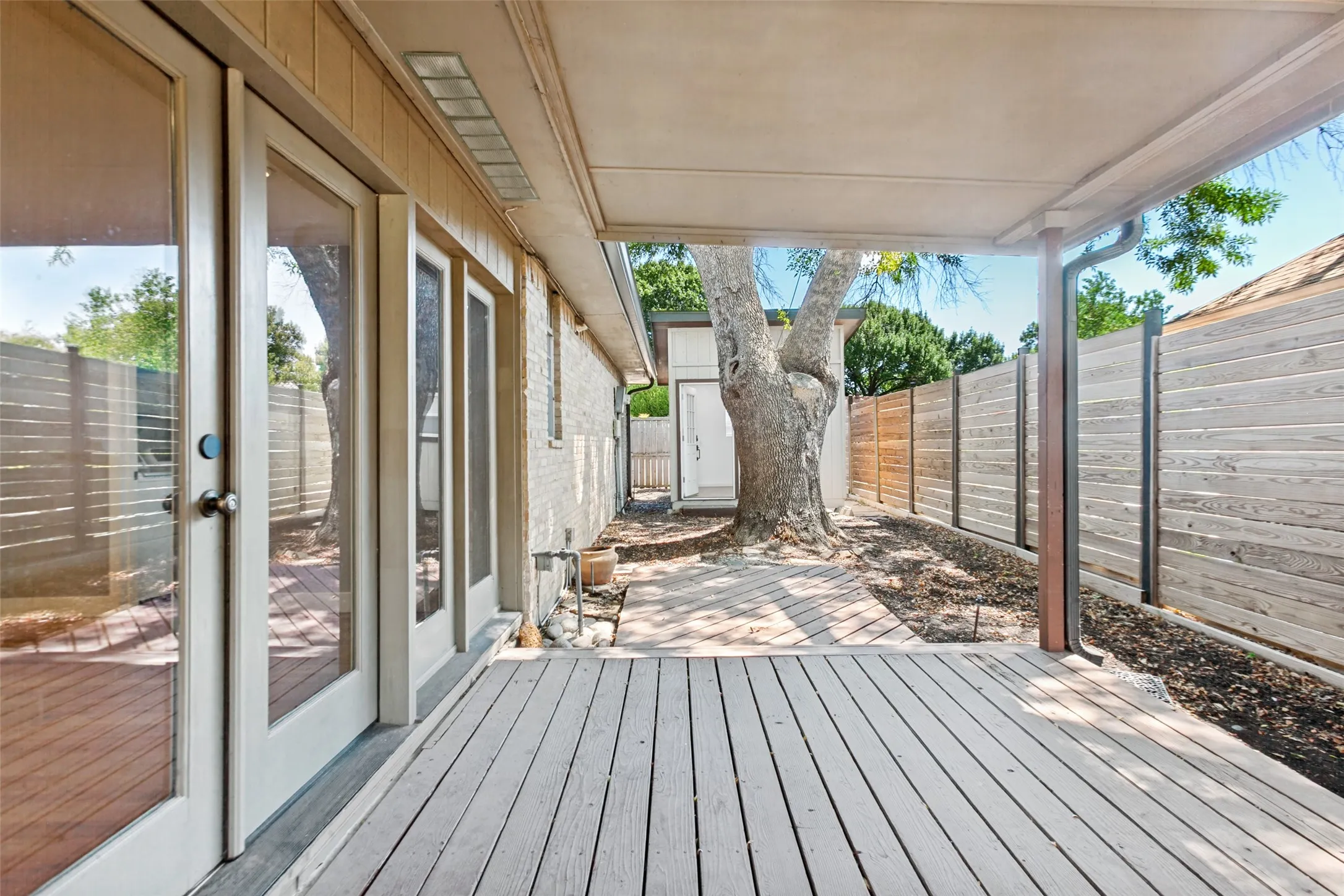 Covered wood deck with multiple glass-paned doors and a wood fence