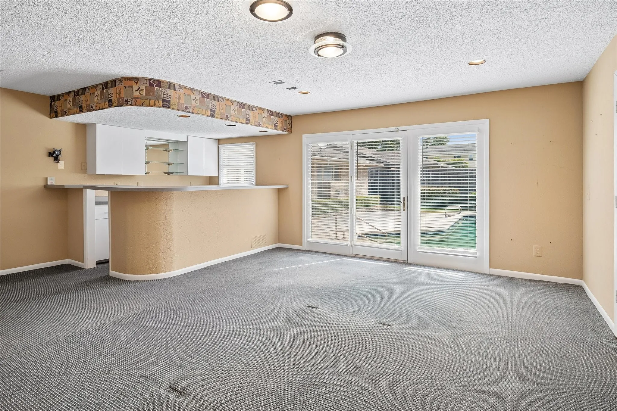Curved built-in wet bar with glass display shelving, plus French doors that open to the pool and patio beyond.