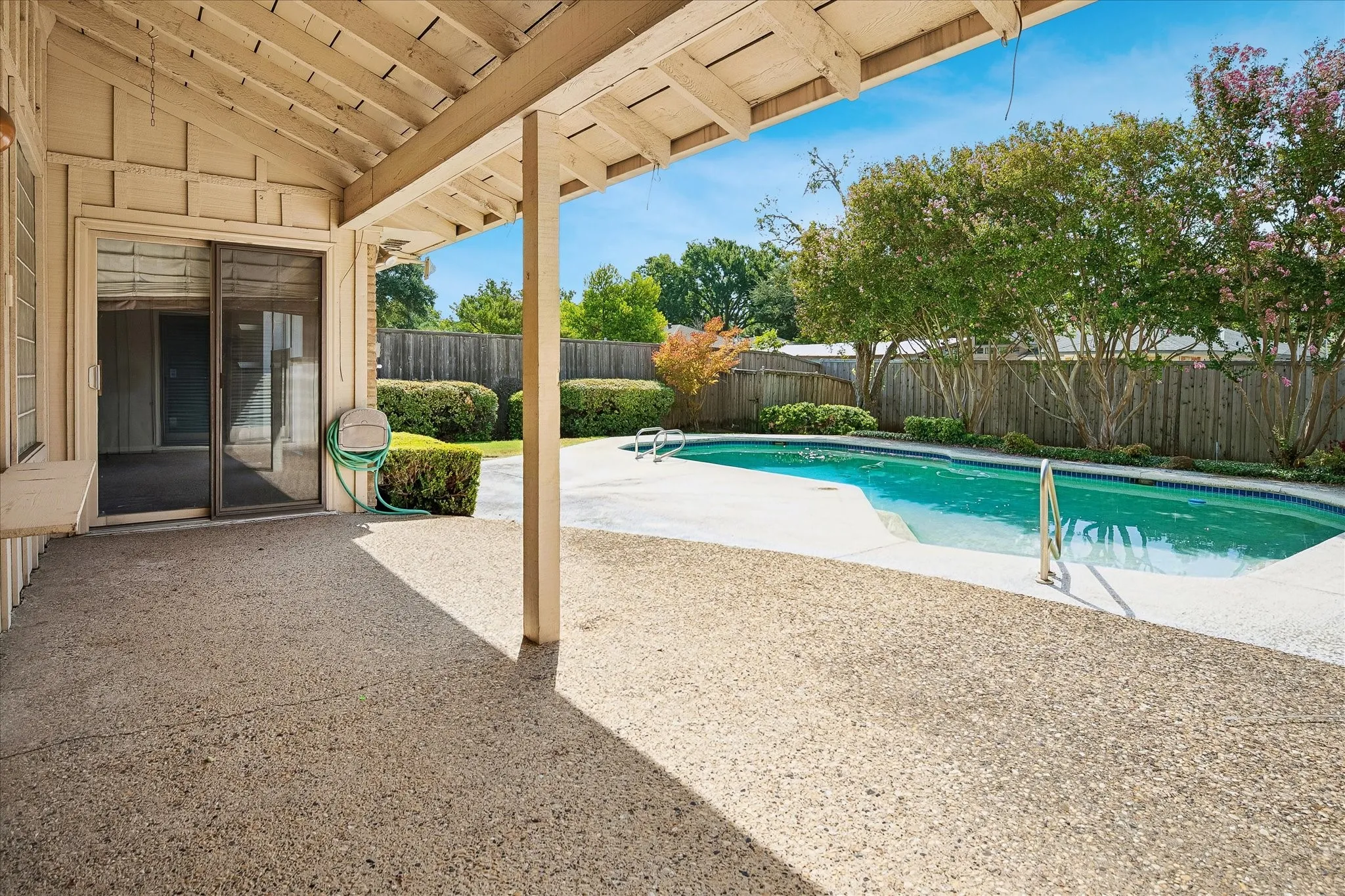 Covered patio overlooking a private, fenced backyard pool surrounded by mature landscaping