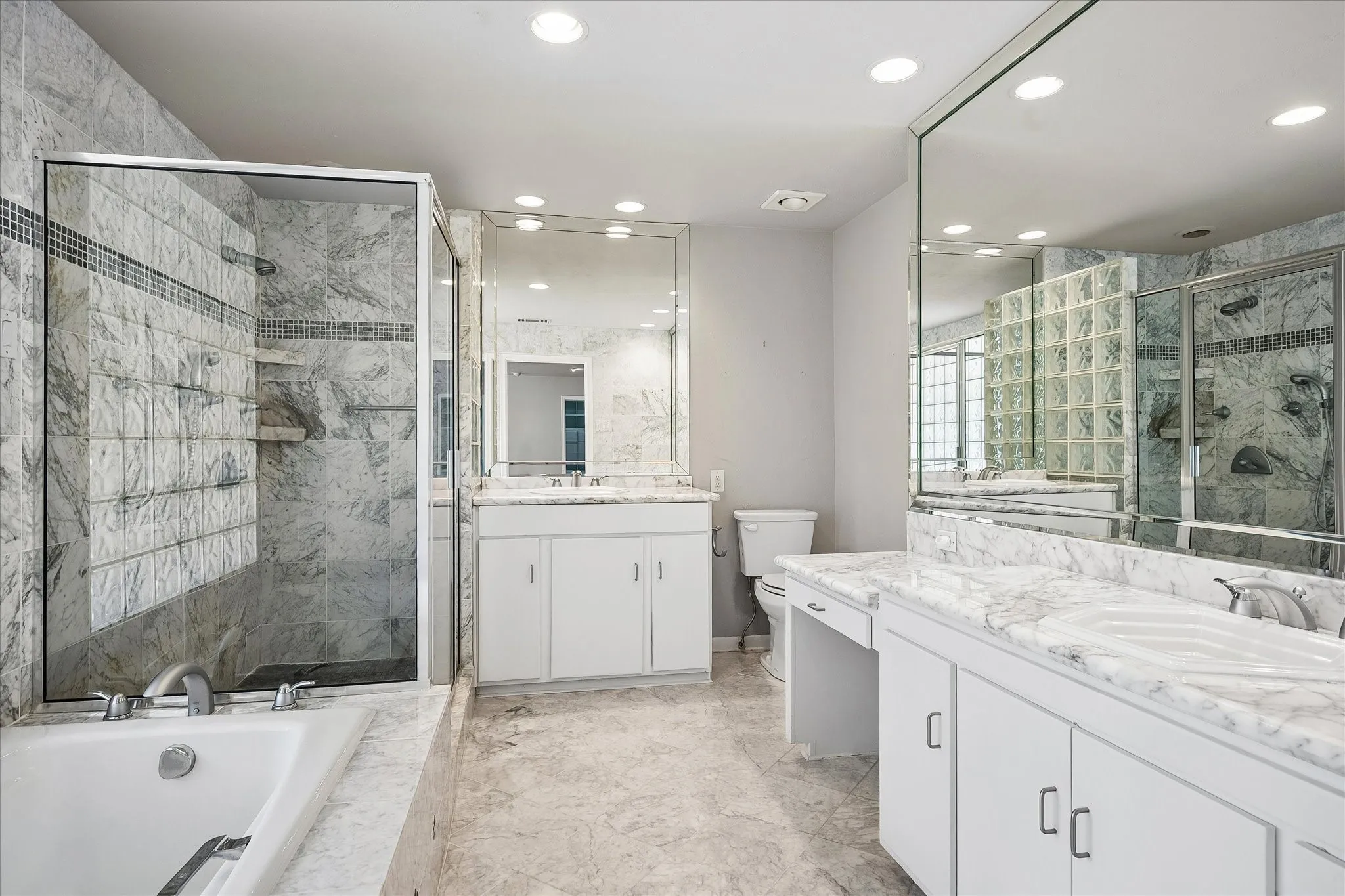 Luxurious marble primary bath with a soaking tub, walk-in glass shower, and dual vanities.