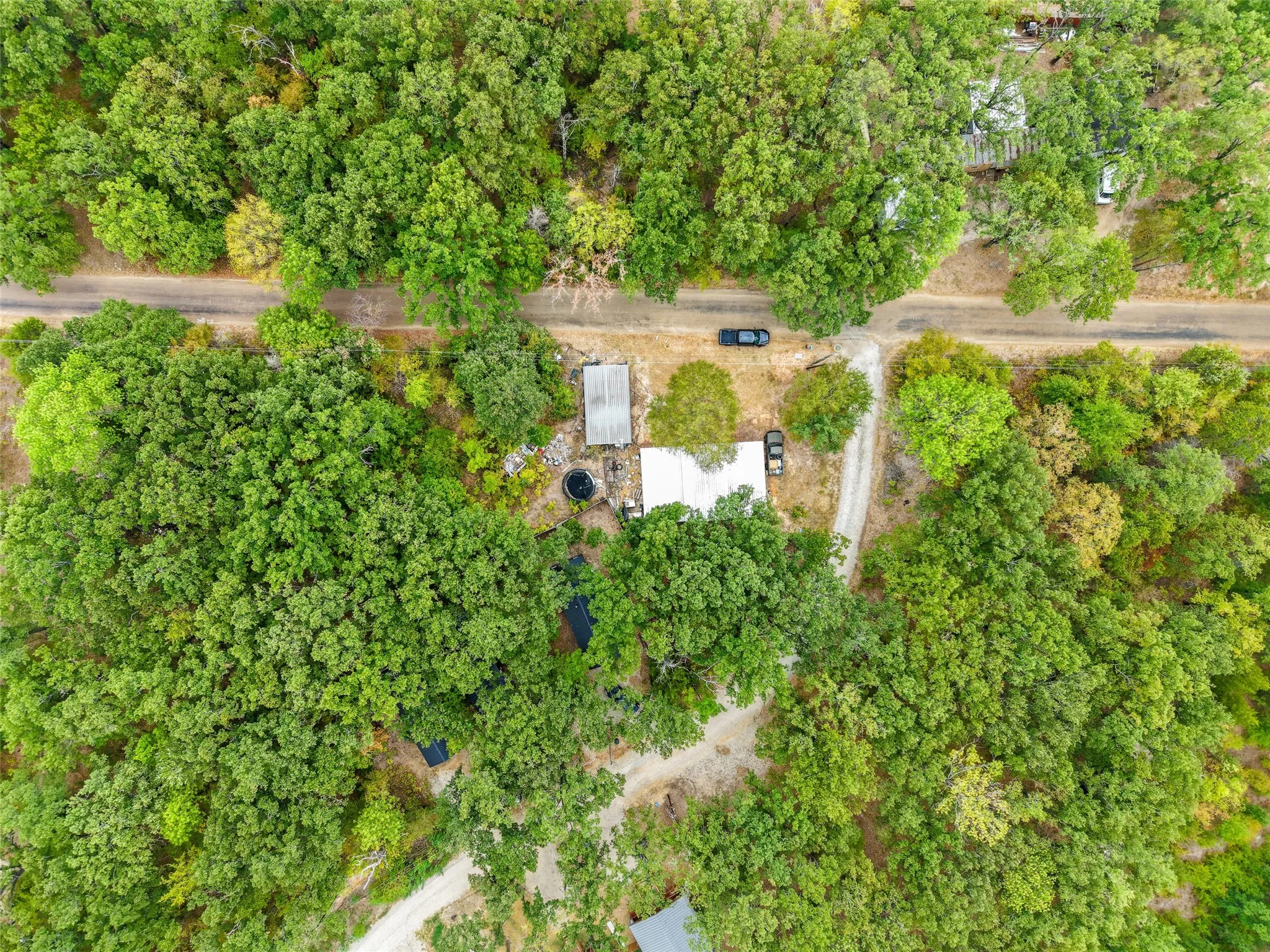 Extensive treed landscape surrounding two distinct structures and a gravel drive