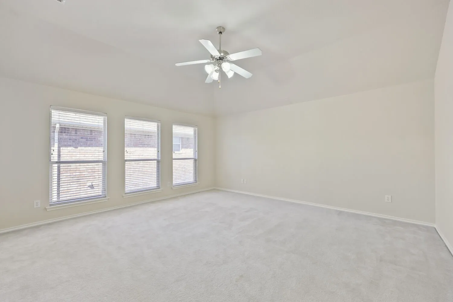 Expansive room featuring vaulted ceilings, three large windows, a ceiling fan with light, and neutral-toned carpeting