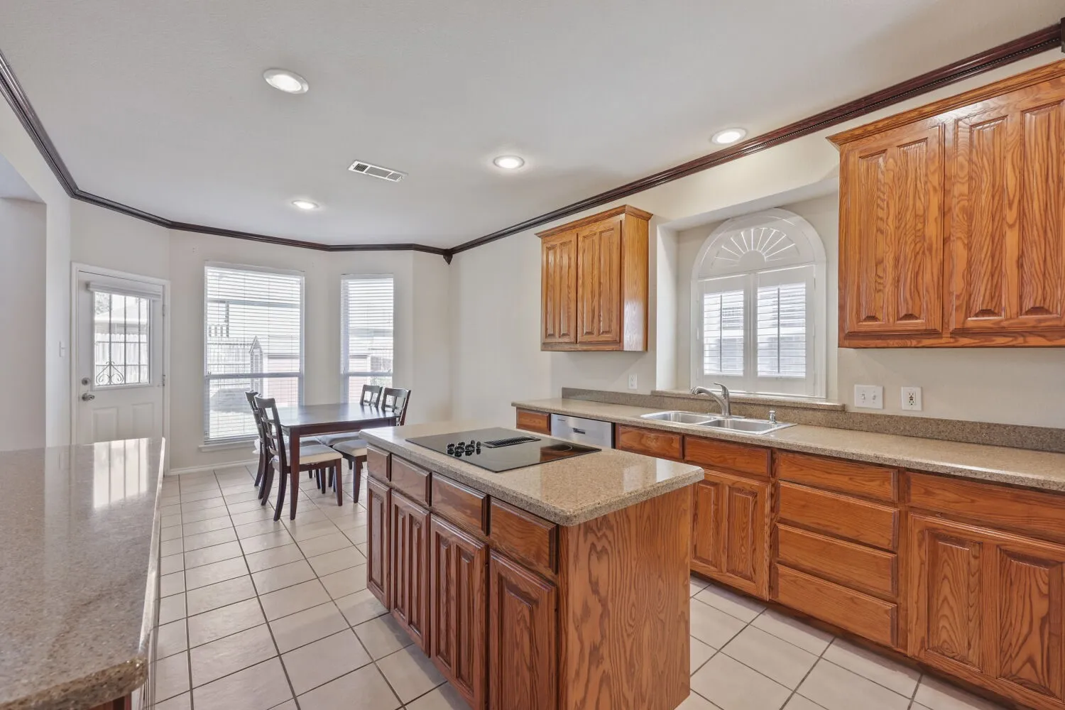 Kitchen featuring recessed lighting, wood cabinetry, stone countertops, a center island with a cooktop, and a bay window with plantation shutters