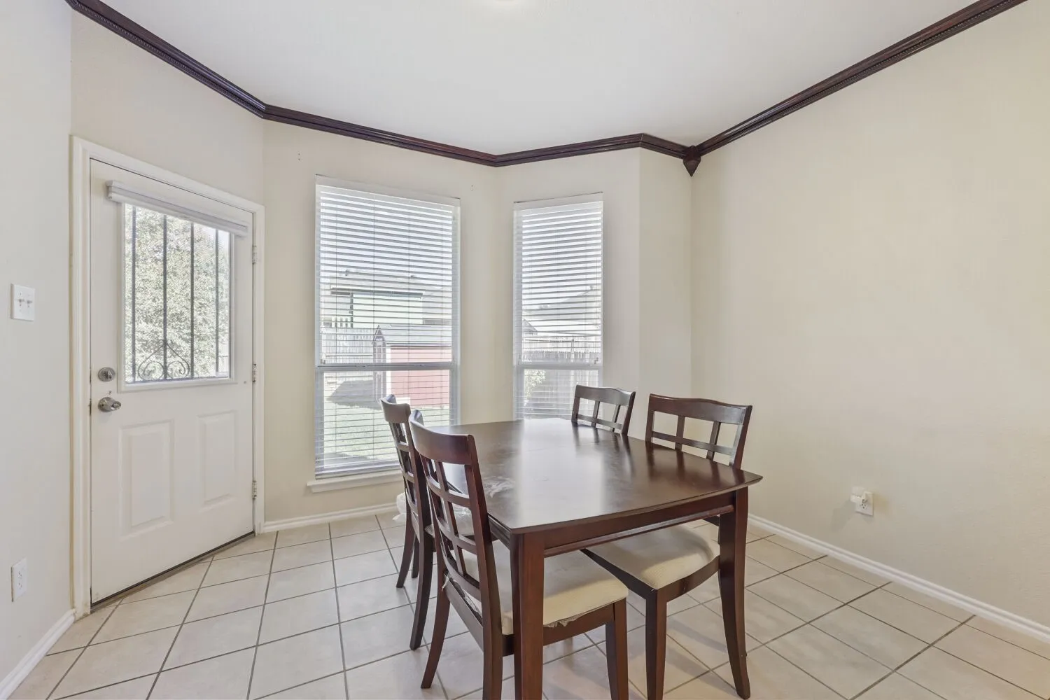 Tiled flooring, multiple windows with blinds, a back exterior door with decorative glass, and contrasting crown molding