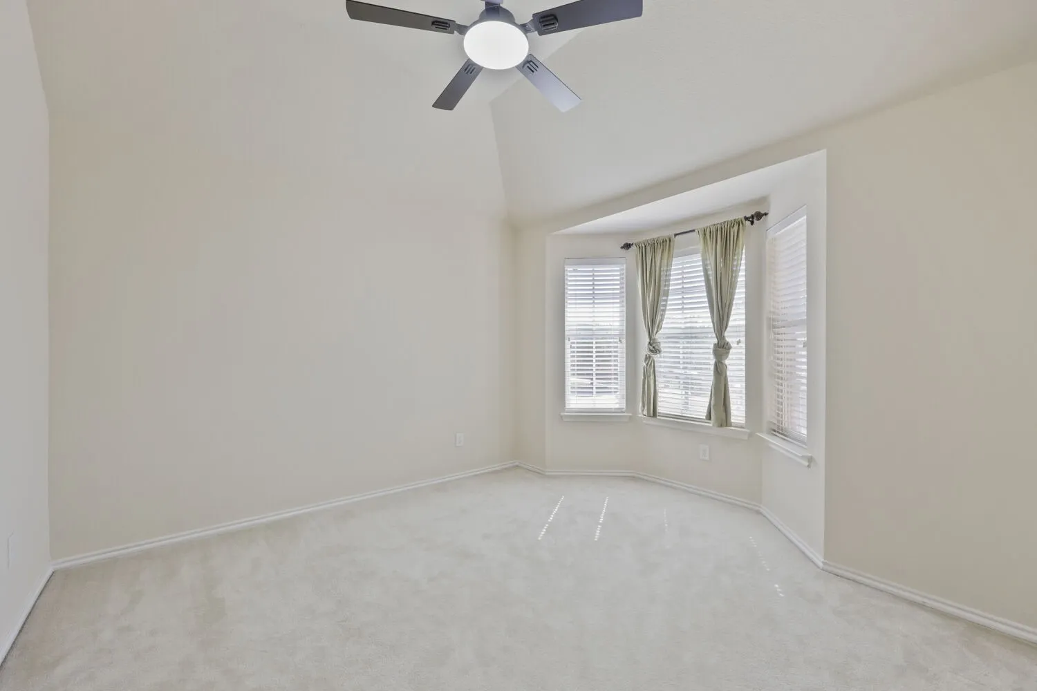 Vaulted ceiling with a ceiling fan, bay window with blinds, and light-toned carpeting