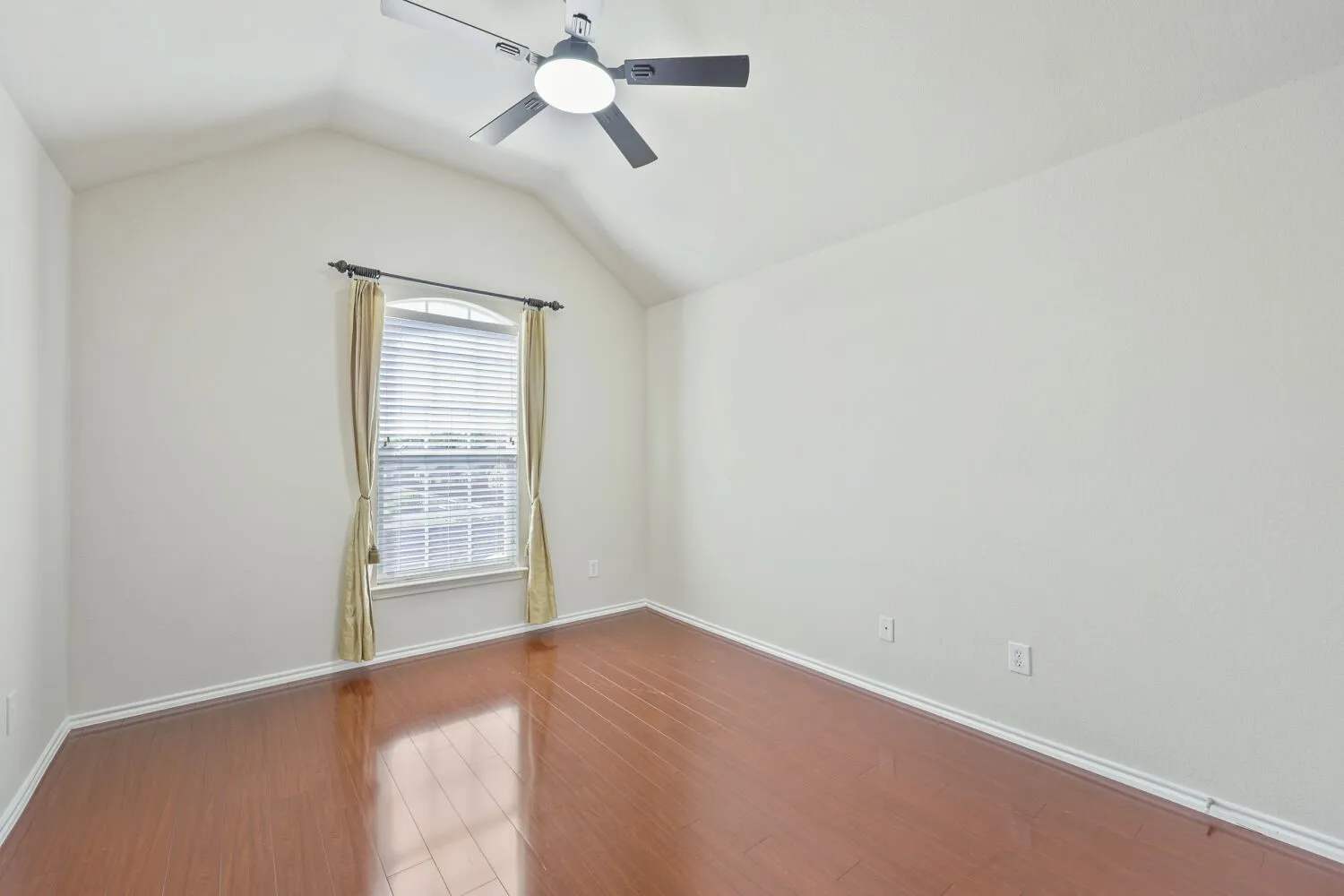 Vaulted ceiling with a ceiling fan, arched window, wood-finish flooring, and white baseboards