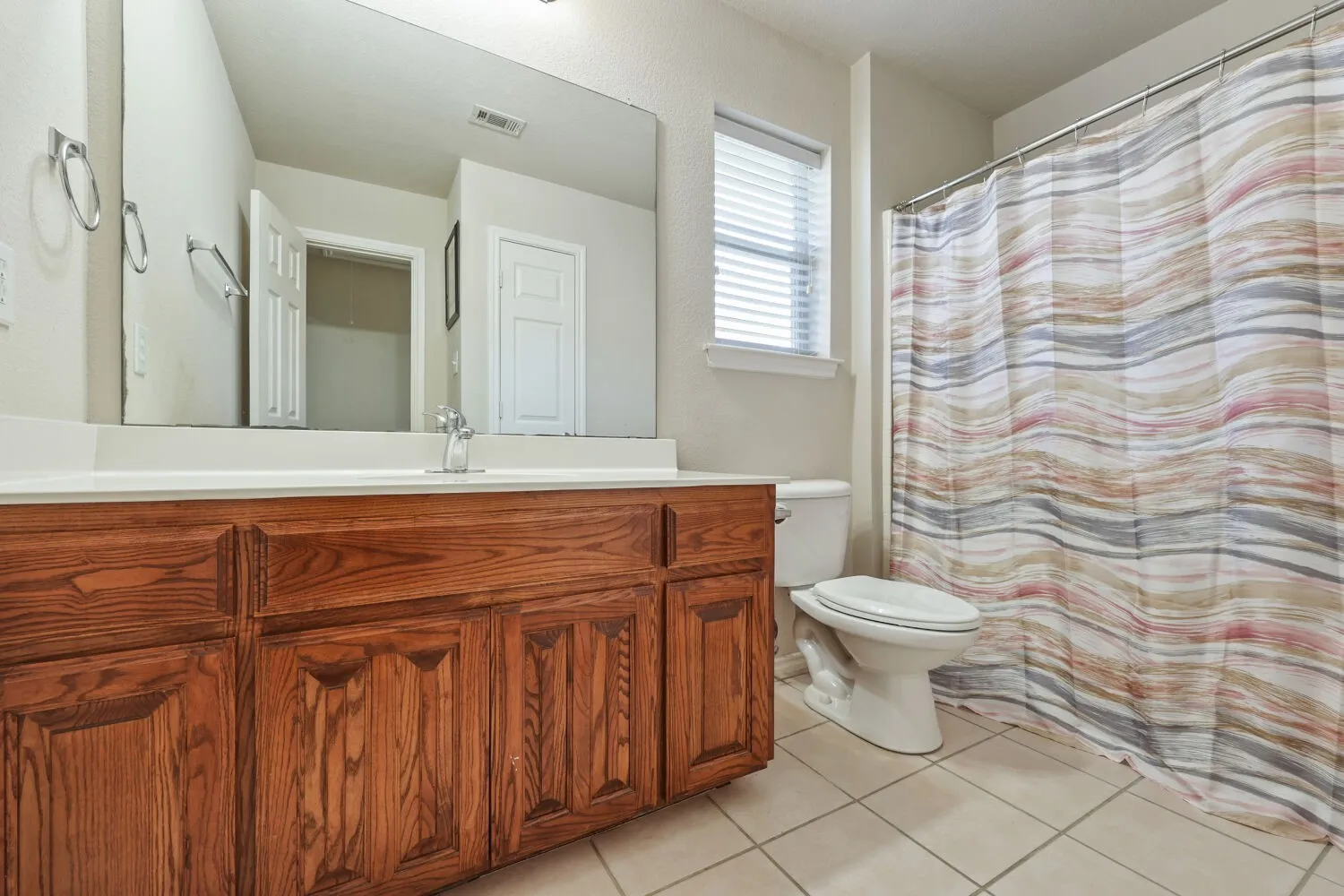 Wood-finish vanity with paneling and a light-toned countertop, integrated sink, and chrome faucet
