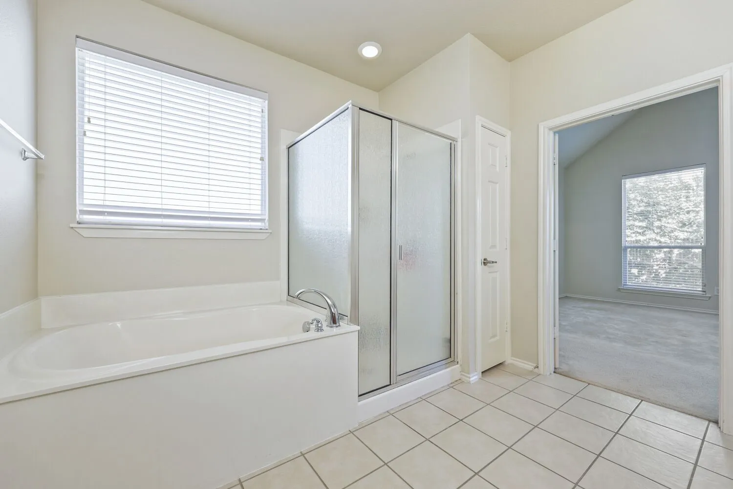 White soaking tub with chrome fixtures, glass-enclosed shower, white tile flooring, and recessed lighting