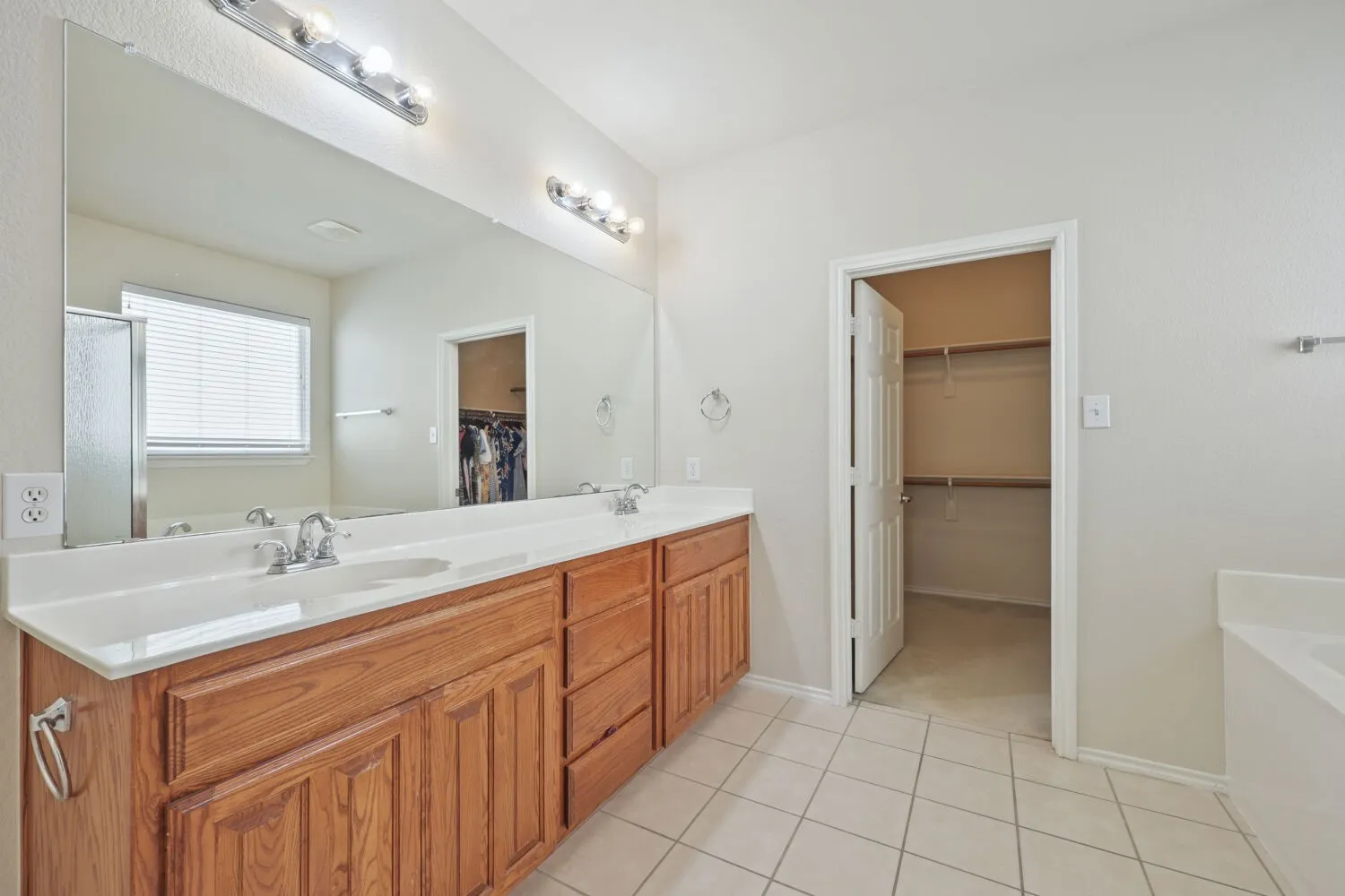 Dual vanity with wood cabinetry, expansive mirror, tile flooring, and separate water closet