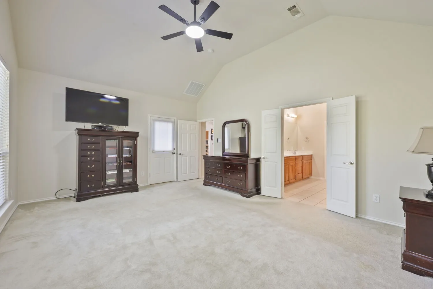 Vaulted ceiling with a ceiling fan, light-toned carpeting, double French doors, and window with blinds