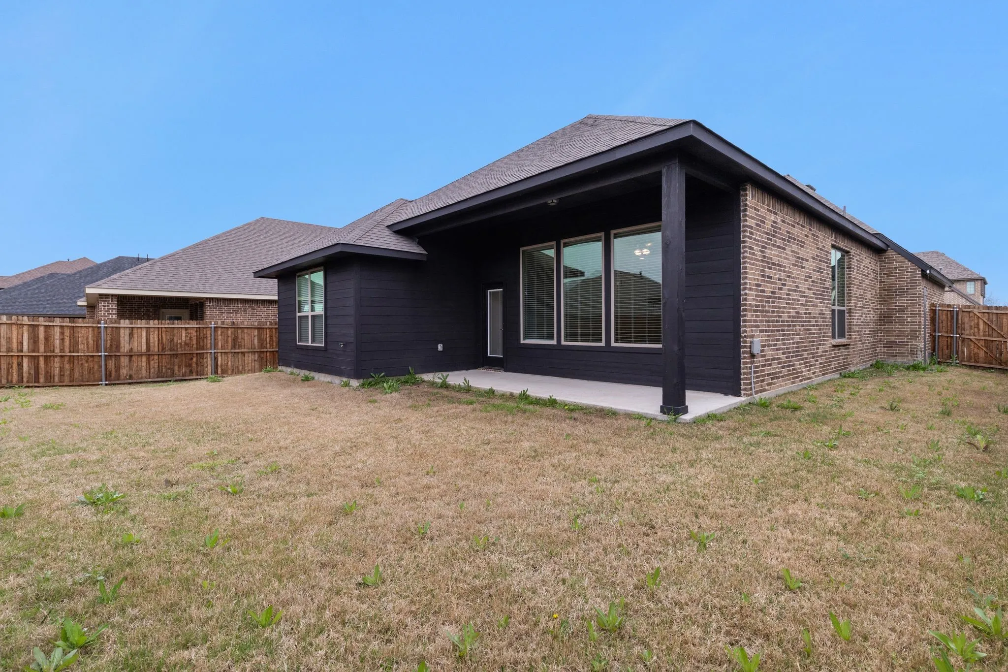 Covered patio with concrete flooring, brick and dark horizontal siding exterior, and multiple large windows