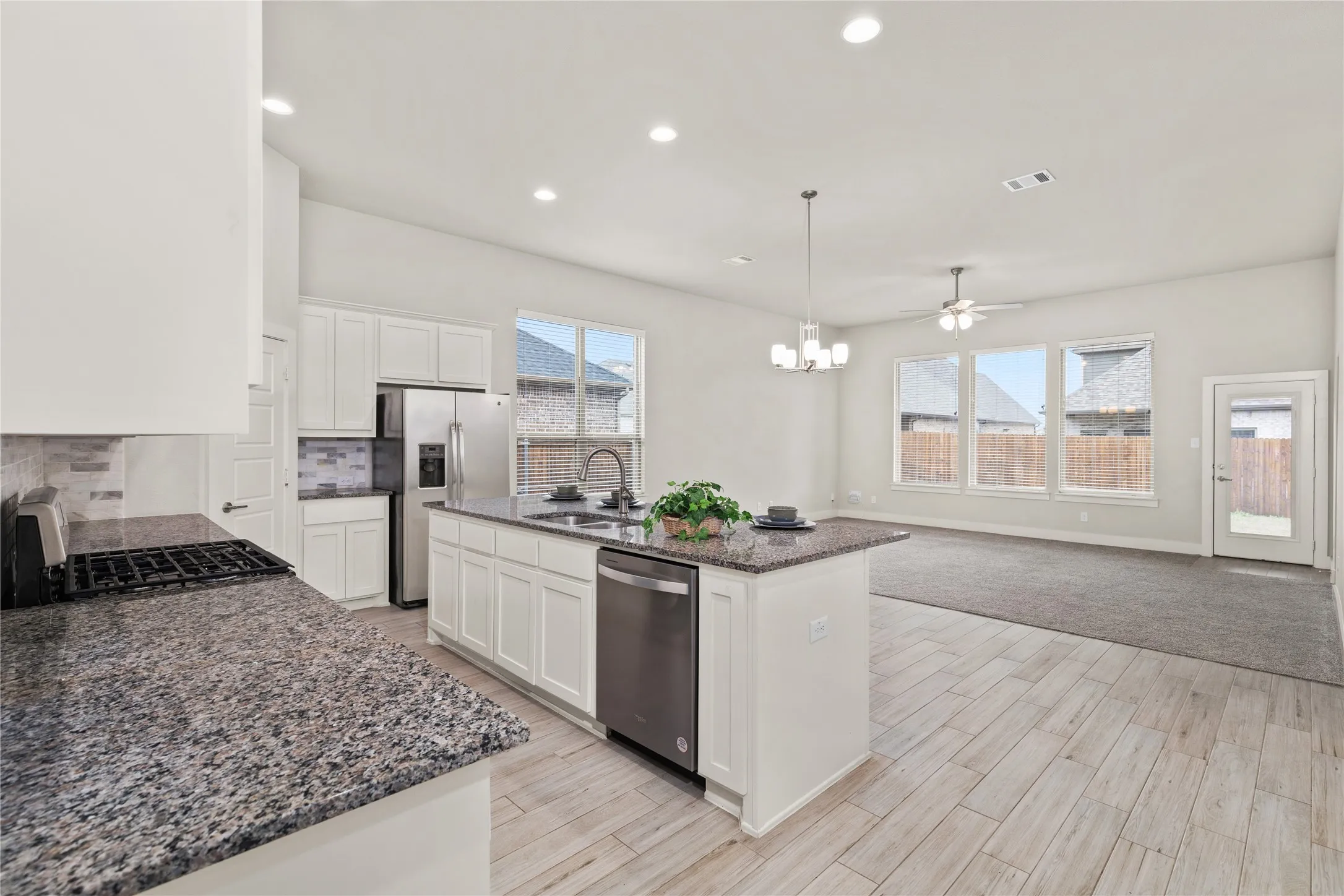 Kitchen island with granite-style countertop, stainless steel appliances, white cabinetry, and wood-finish flooring