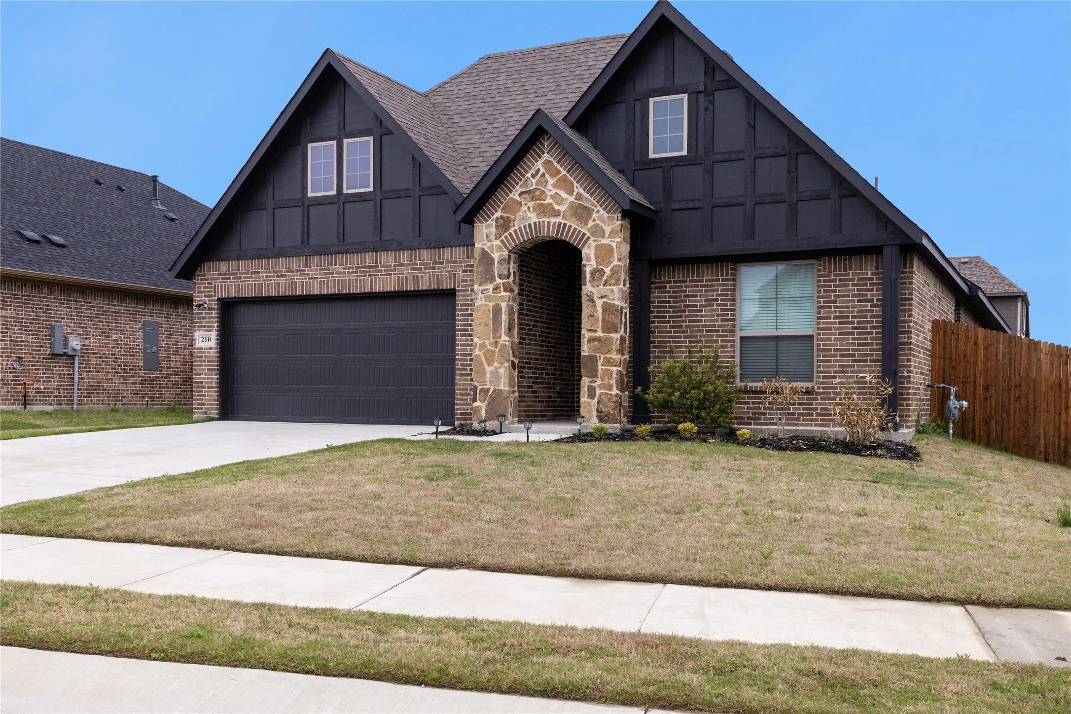 Brick and stone exterior with dark facade trim, arched stone entry, and attached garage