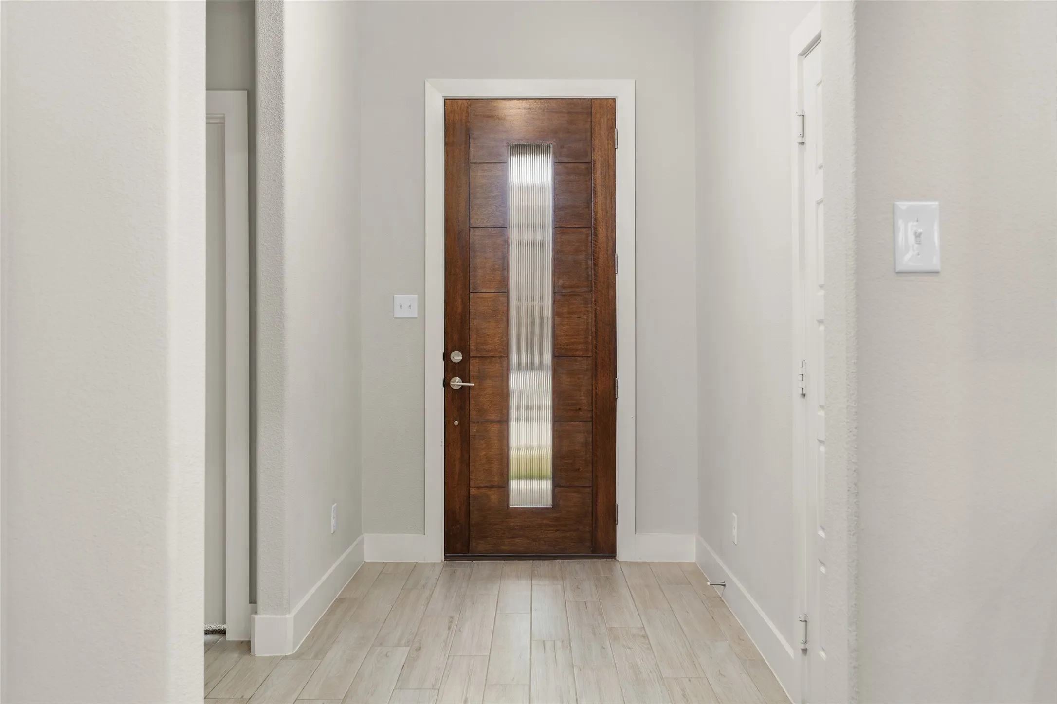 Wood-finish flooring leading to a wood-paneled door with a glass insert