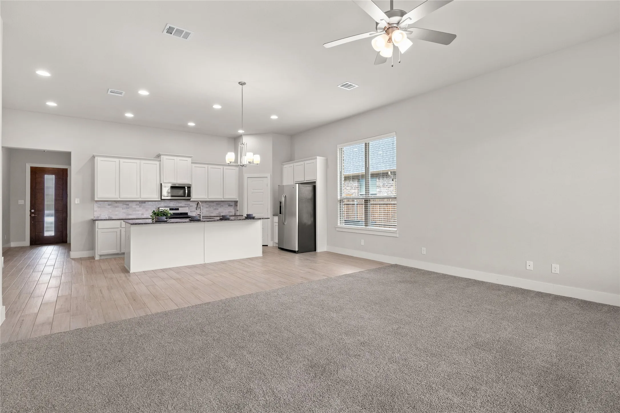 Open-concept living space featuring a kitchen with white cabinetry, stainless steel appliances, a center island, and recessed lighting
