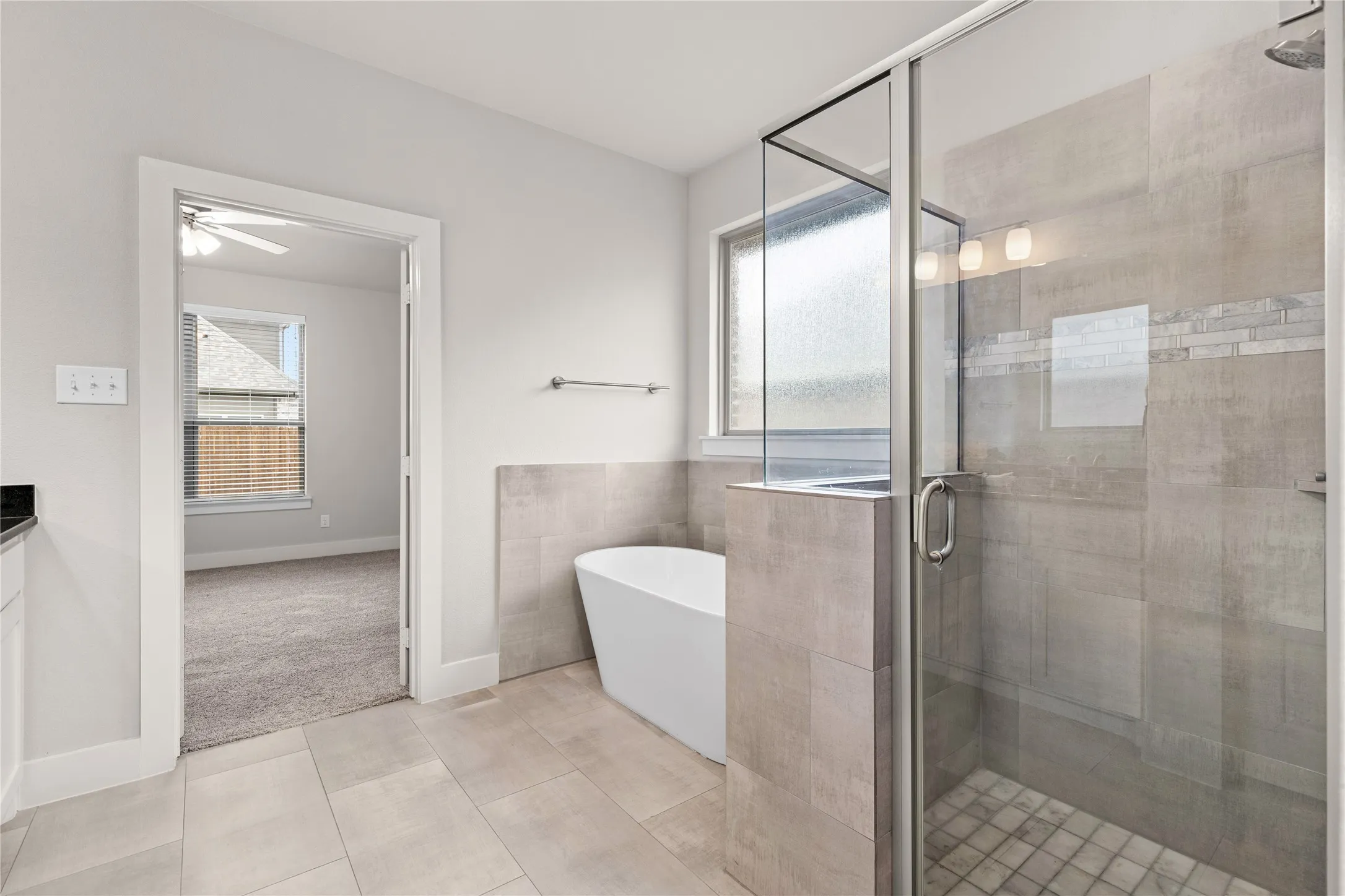 Freestanding soaking tub, walk-in shower with glass enclosure, tiled shower walls with decorative accent, tile flooring, and a vanity with a dark countertop