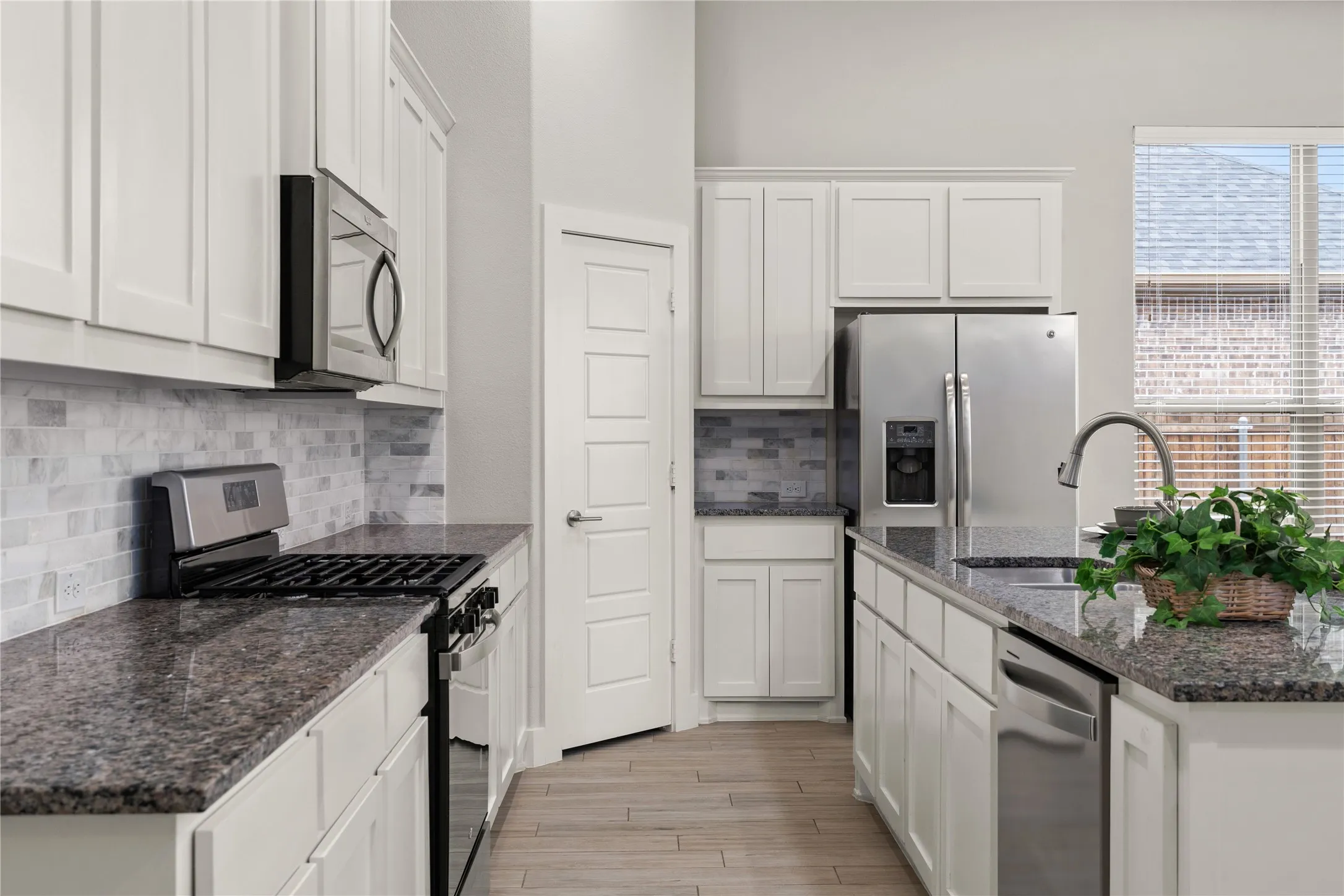 Kitchen featuring white cabinetry, granite countertops, tile backsplash, stainless steel appliances, and wood-finish flooring