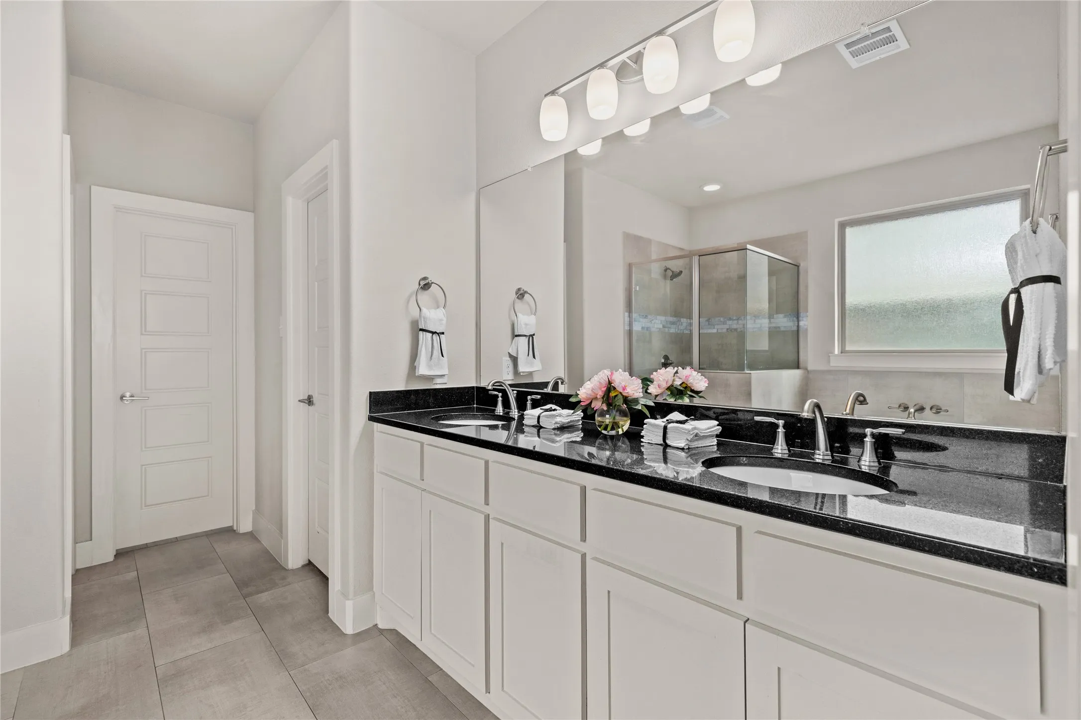 Dual vanities with dark countertops, a large mirror, shower enclosure, and soaking tub