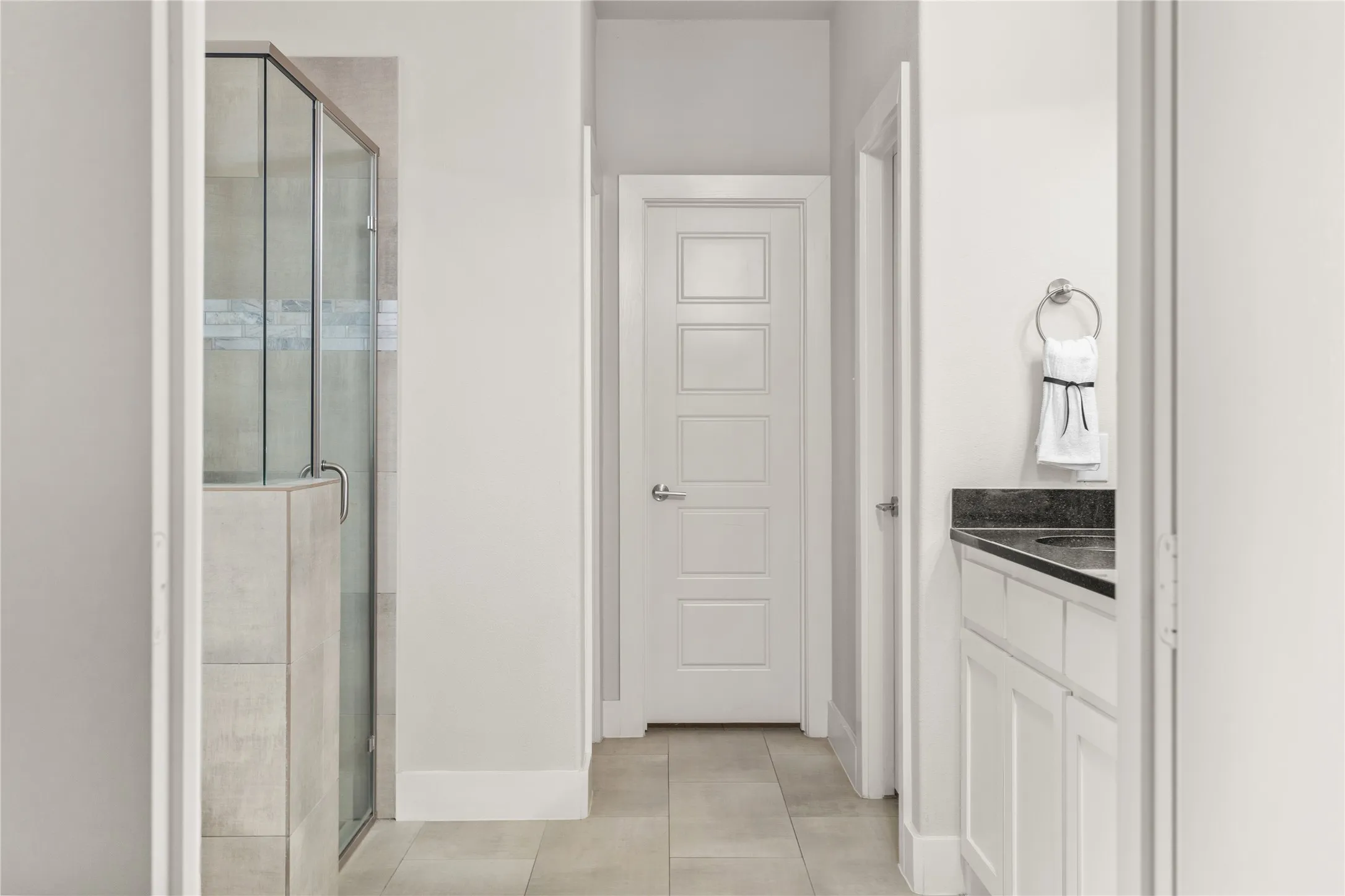 Glass-enclosed shower with tile surround and integrated ledge, tile flooring, white paneled door, and vanity with dark countertop