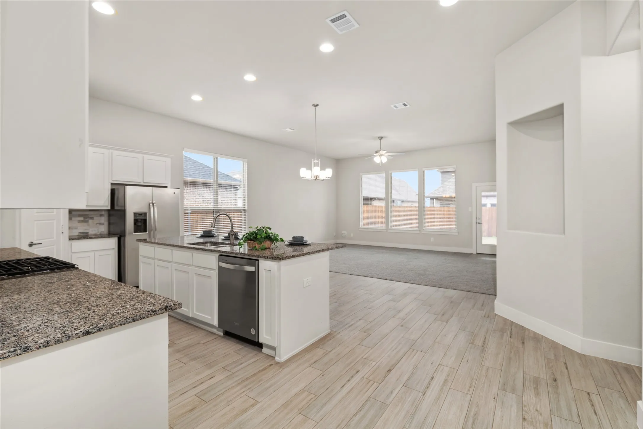 Open-concept living area with wood-finish flooring, recessed lighting, and a kitchen island featuring a sink and dishwasher