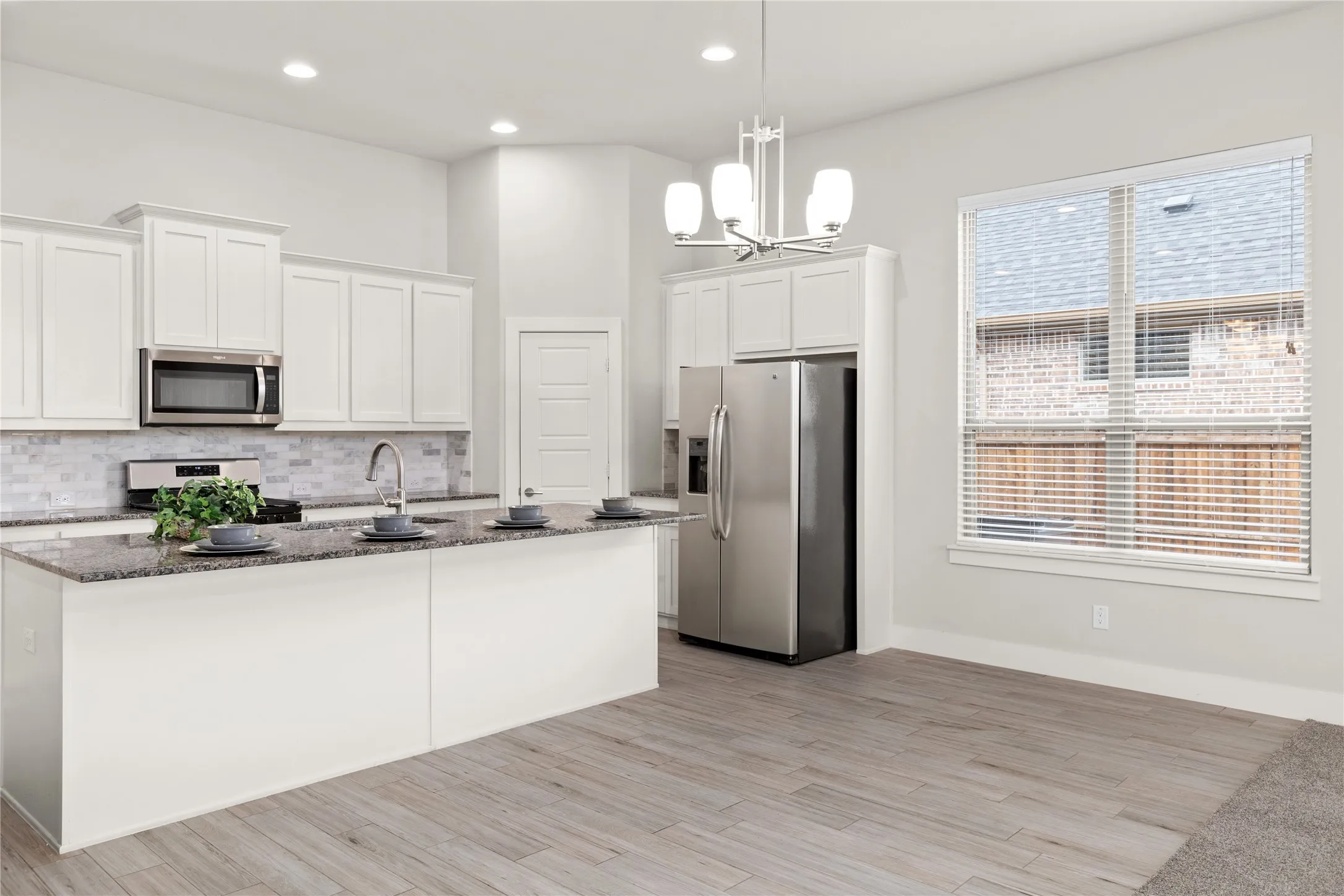 Kitchen featuring white shaker cabinetry, stainless steel appliances, a large island with a sink, and pendant lighting