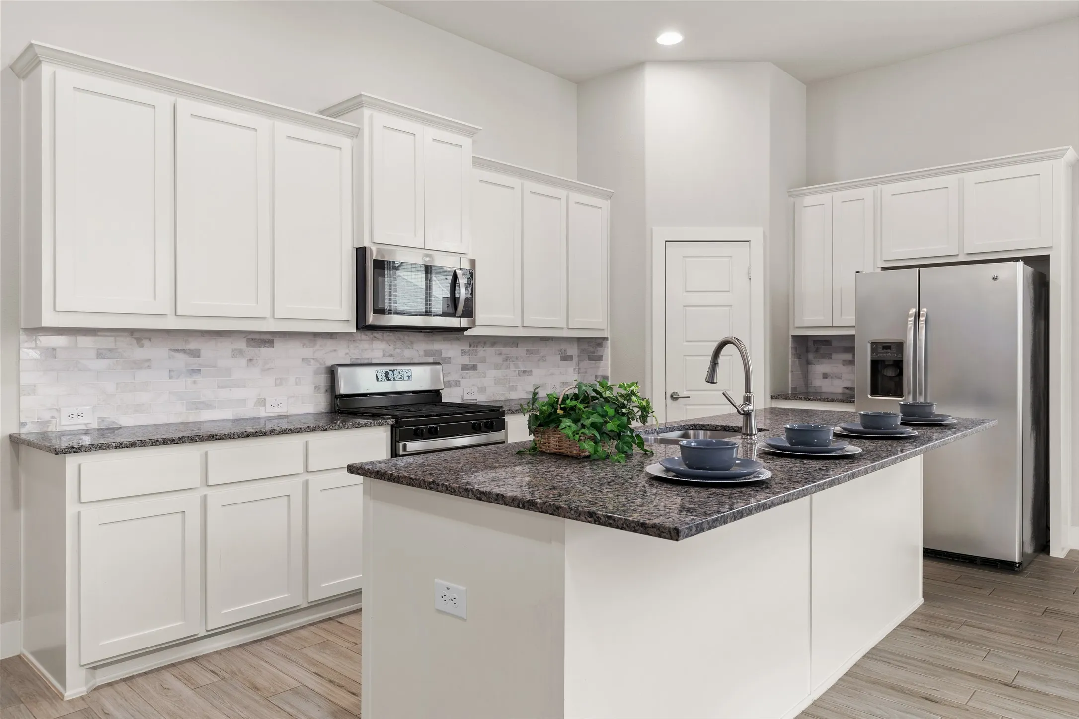 Sleek kitchen featuring white cabinetry, stainless steel appliances, dark stone countertops, a tiled backsplash, and wood-finish flooring