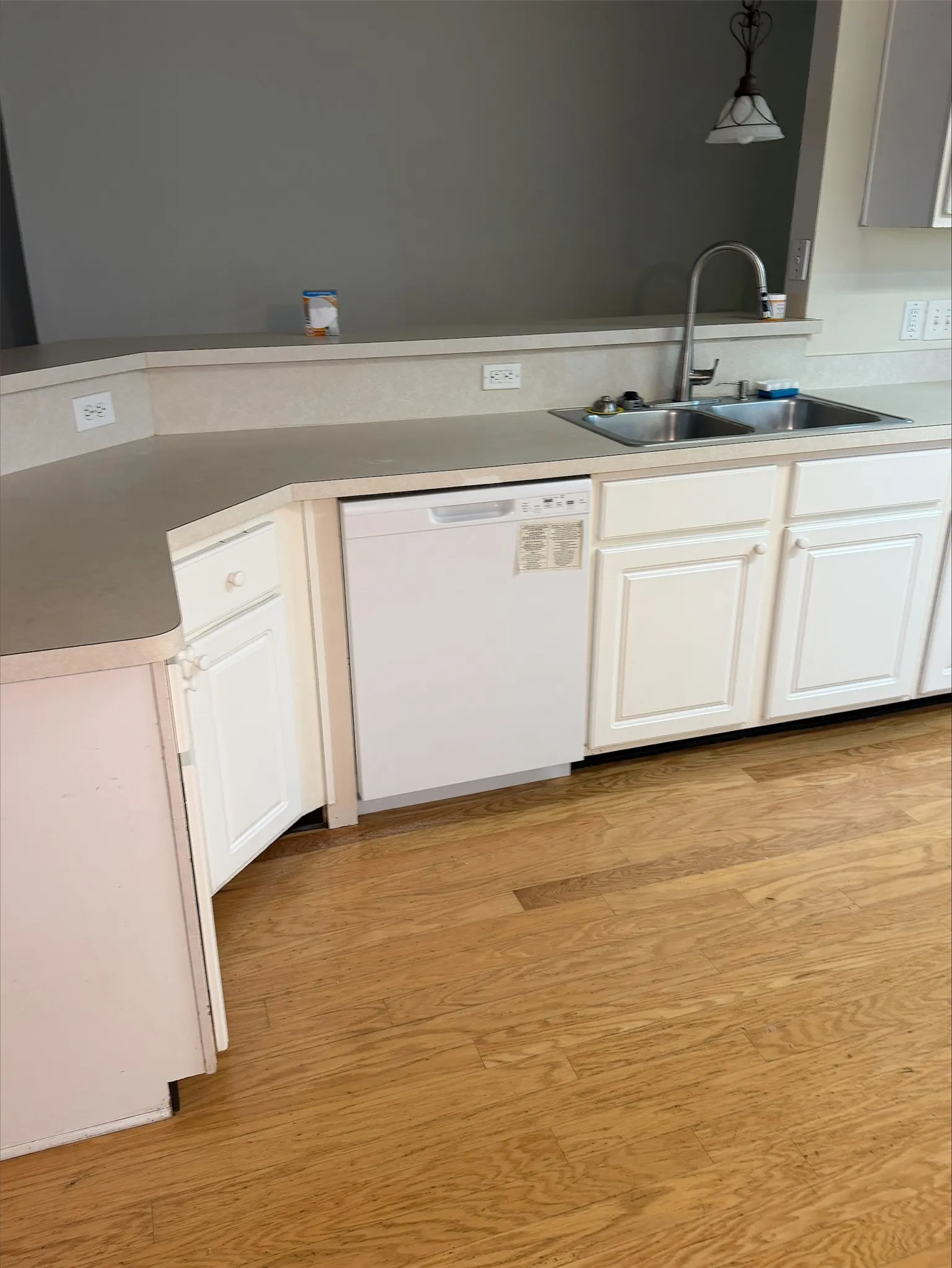 Kitchen featuring white cabinetry, dual basin sink with gooseneck faucet, light-toned countertops, and wood-finish flooring