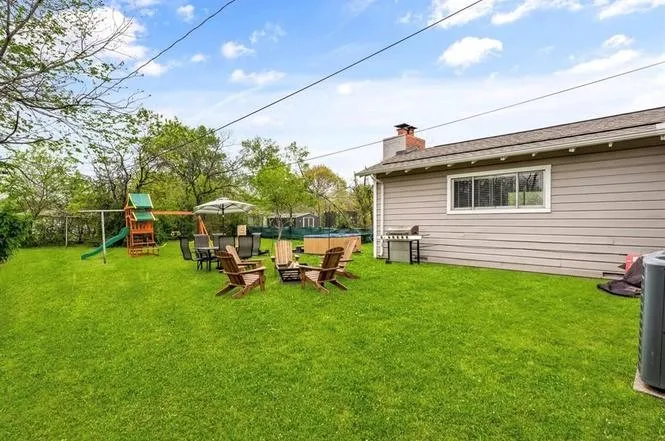 Expansive grassy yard with mature perimeter trees, featuring a stucco-sided exterior and a brick chimney