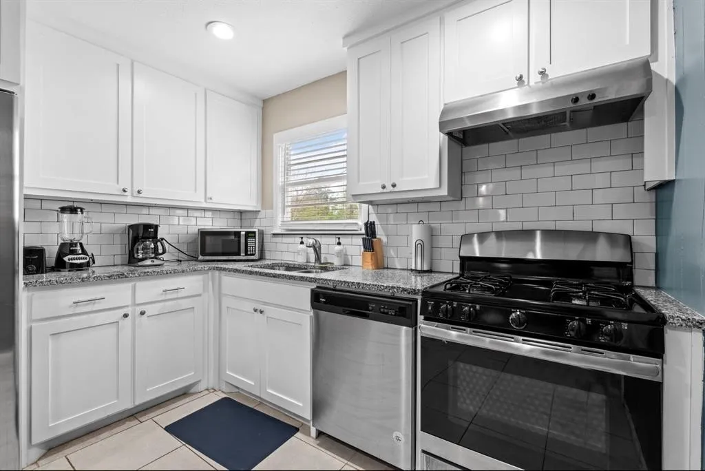 White shaker cabinetry with polished chrome hardware, light-toned countertop, stainless steel appliances, subway tile backsplash, and light-toned floor tile