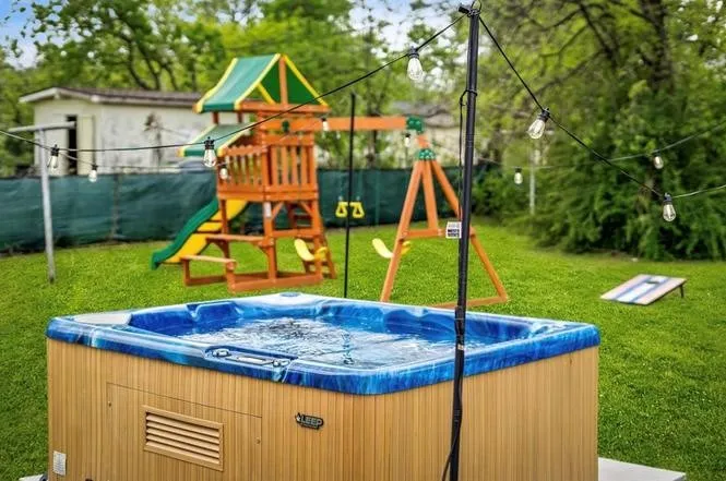 Expansive green lawn featuring a built-in hot tub with wood-finish siding, a multi-level playset, and string lighting