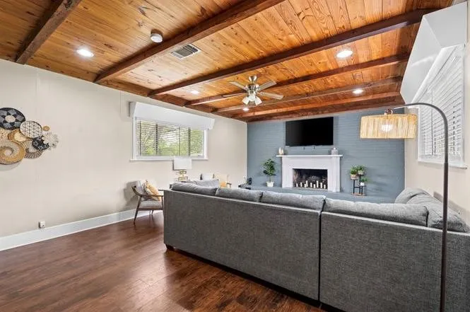 Wood-finish flooring, exposed wood beam ceiling, recessed lighting, ceiling fan, and a painted brick fireplace