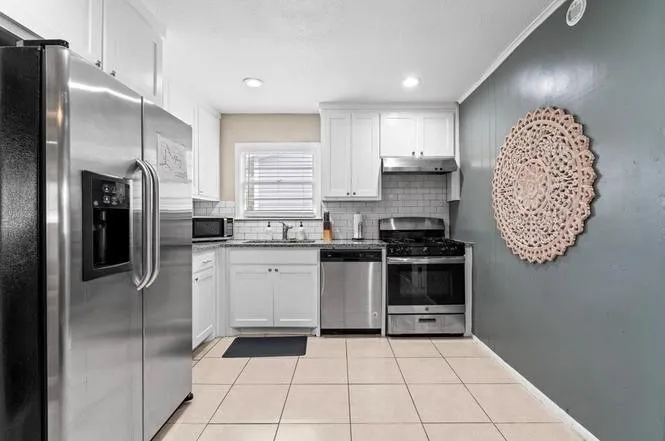Kitchen featuring white cabinetry, tile flooring, stainless steel appliances, a subway tile backsplash, and a window with blinds