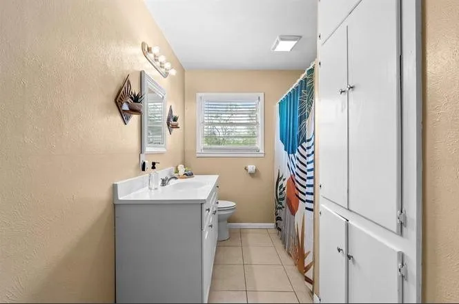 White vanity with integrated sink, rectangular mirror, light fixture, window with blinds, and built-in storage cabinets