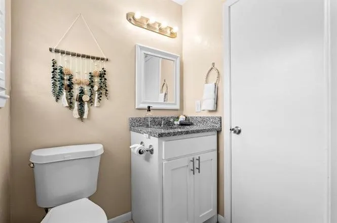 White vanity with shaker-style cabinetry, a gray speckled countertop, and a white framed mirror