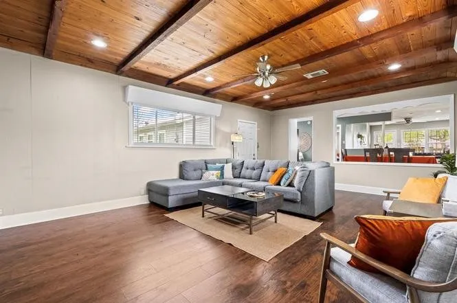 Exposed wood beam ceiling with recessed lighting, wood-finish flooring, a ceiling fan, and a pass-through window to an adjacent room