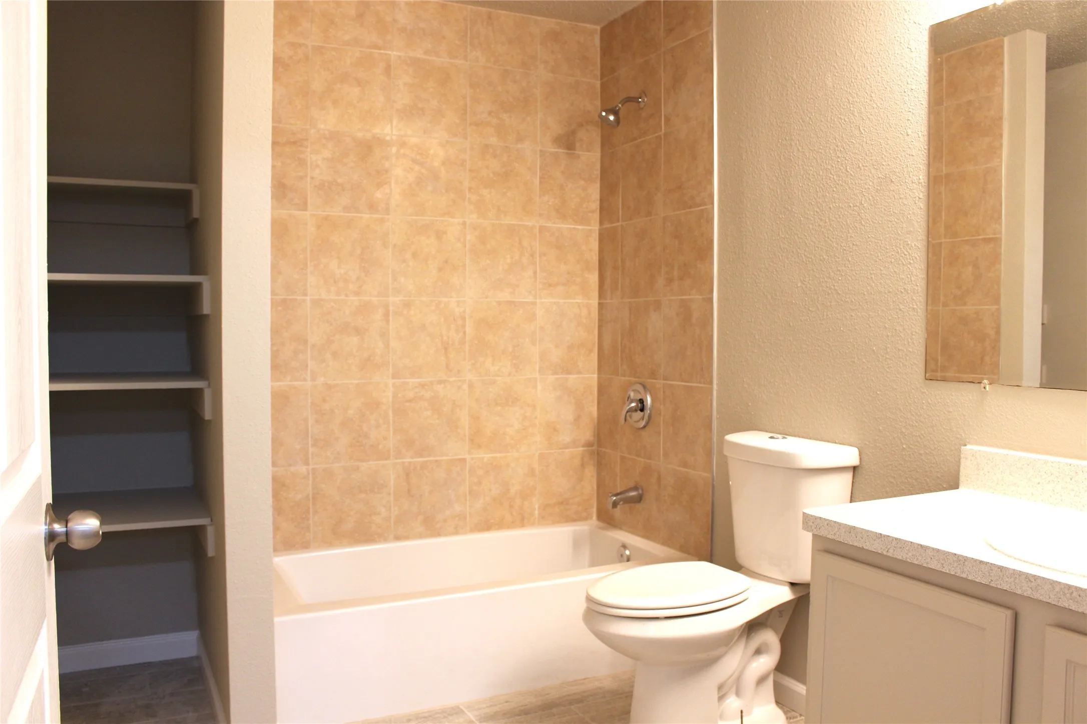 Tile flooring, built-in shelving, tile shower surround, shower/tub combination, and a vanity with an integrated sink